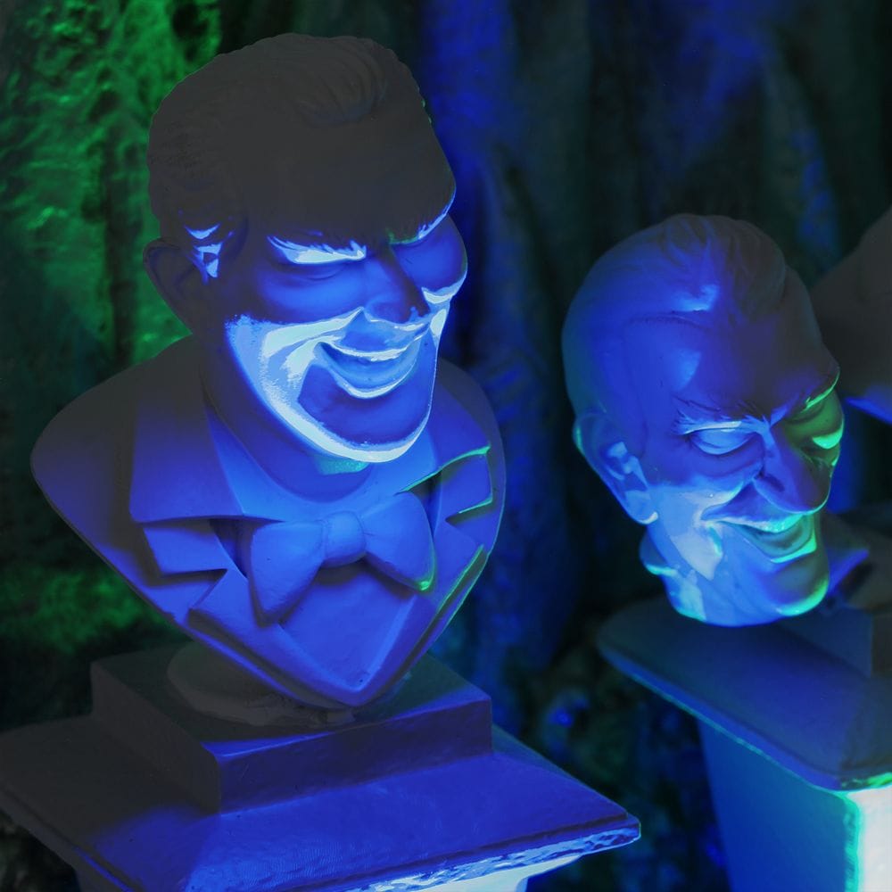 Two eerie, grinning busts from the Haunted Mansion Collection glow with blue and green light, creating a spooky atmosphere.
