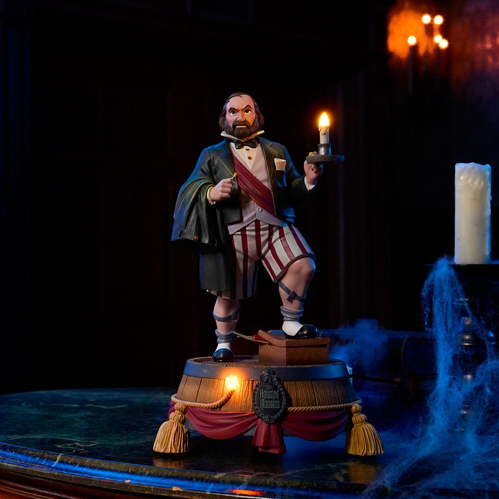 A statue of a man in striped pajamas holding a lit candle, part of the Haunted Mansion Collection, in a dimly lit room.