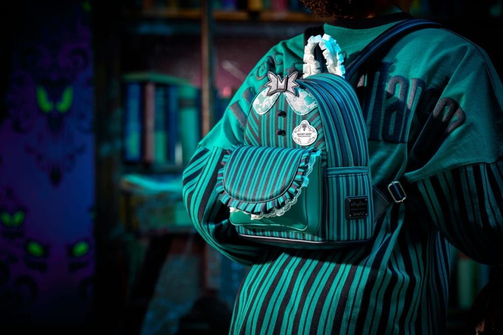 Person wearing a teal-striped shirt and mini backpack in a dimly lit, book-filled Disney Store inspired by Haunted Mansion vibes.