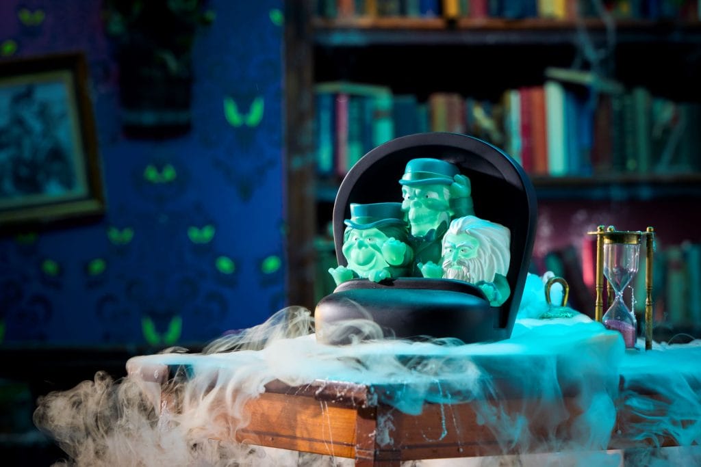 Three green ghost figurines ride in a black carriage, inspired by Disney Store’s Haunted Mansion, on a foggy table.