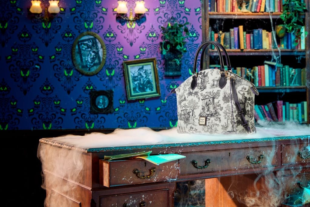 White and black designer handbag on a smoky desk in a haunted mansion library with eerie purple wallpaper.