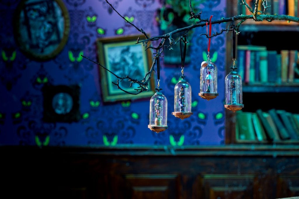 Four glass ornaments hang from a bare branch, echoing Haunted Mansion vibes in a room with vintage decor.