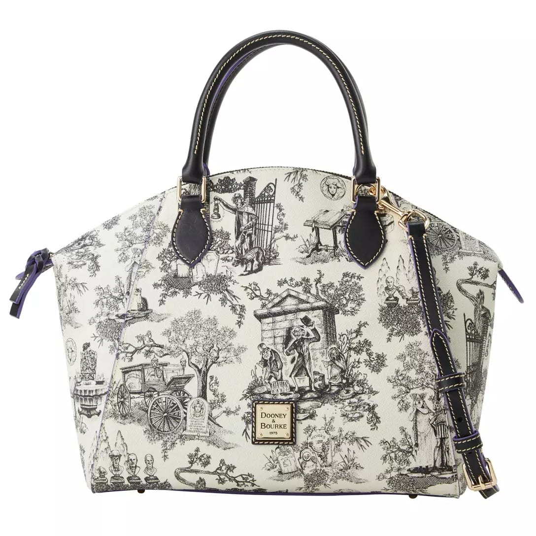 White satchel handbag with black Haunted Mansion toile print, black handles, and gold Dooney & Bourke logo plate.