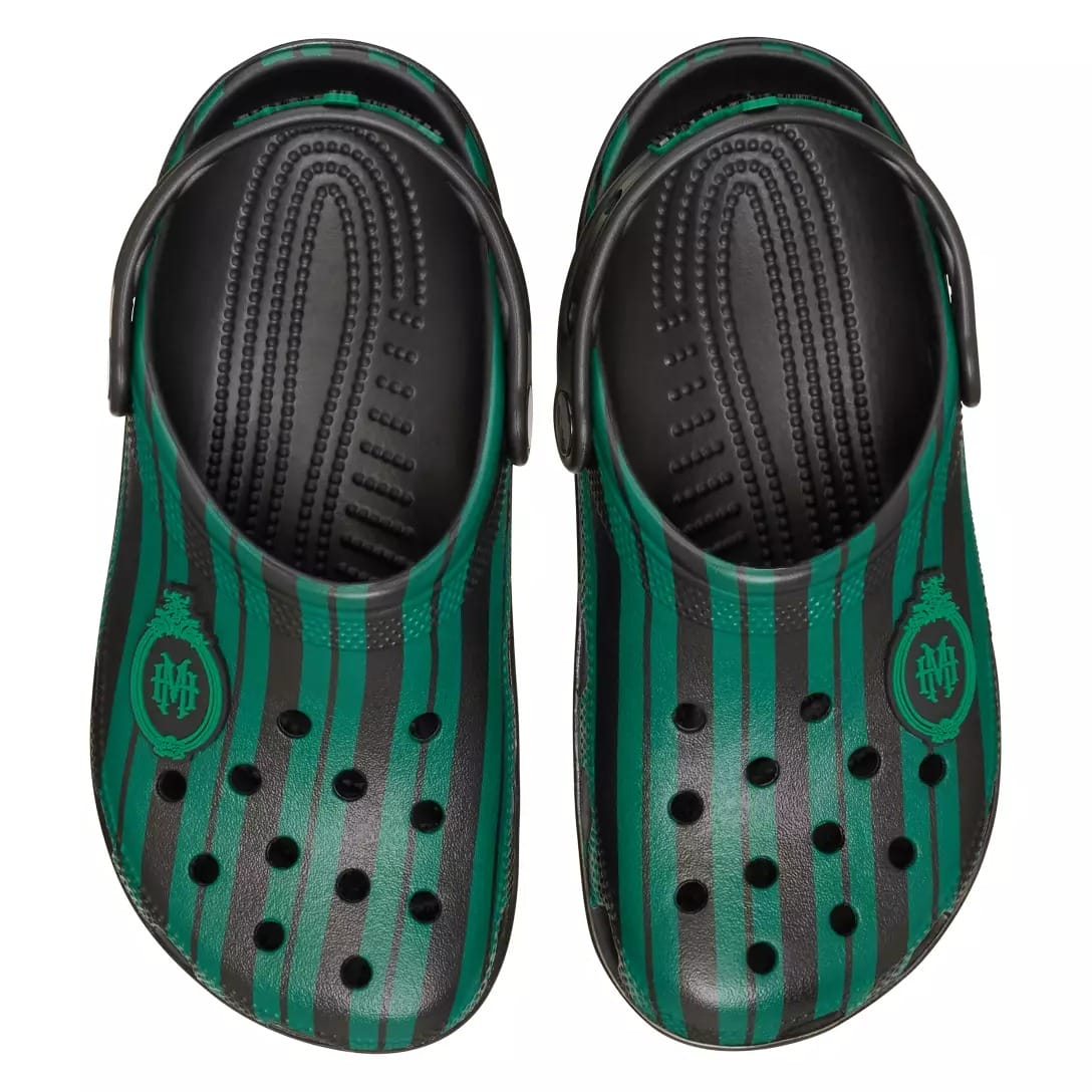 A pair of black and green striped Crocs from the Haunted Mansion Collection with the Slytherin crest on the sides.