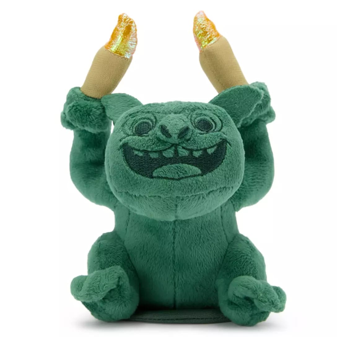 Plush green gremlin toy smiling with arms raised, holding two sparkling gold candles from the Haunted Mansion Collection.