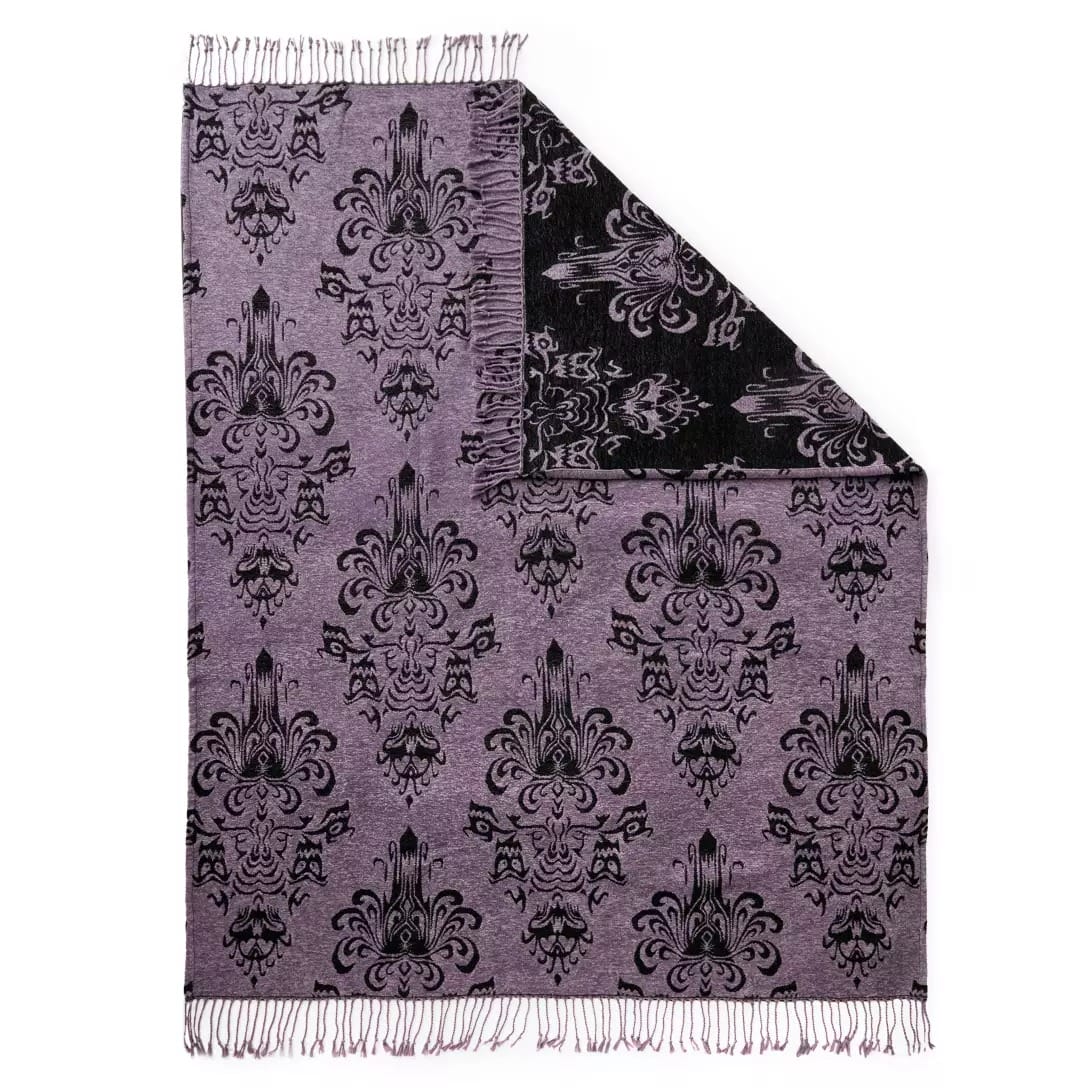 Purple and black blanket with a damask pattern from the Haunted Mansion Collection, fringed edges, and folded corner.