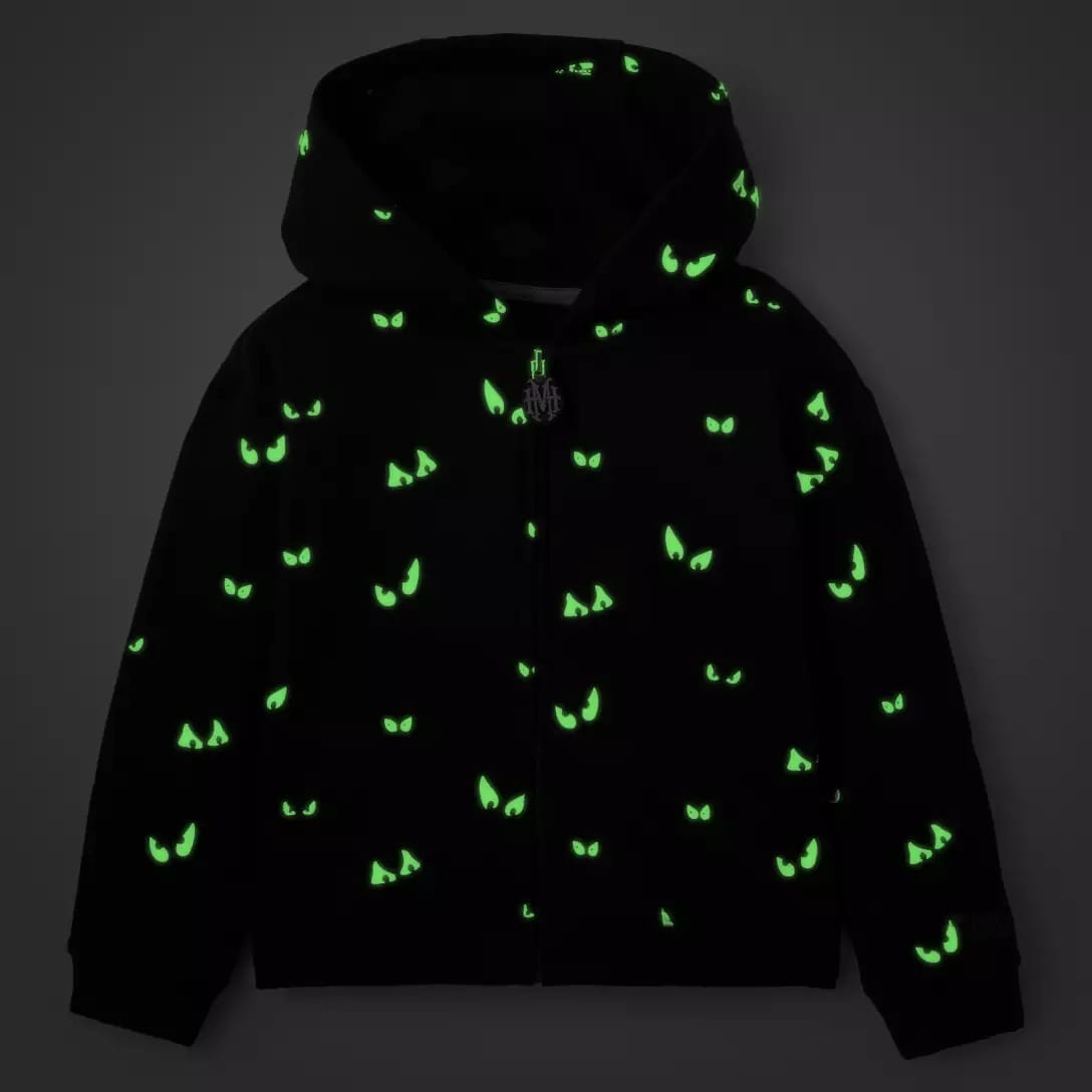 Black hoodie with hood up, part of the Haunted Mansion Collection, features glowing green eyes scattered across the fabric.
