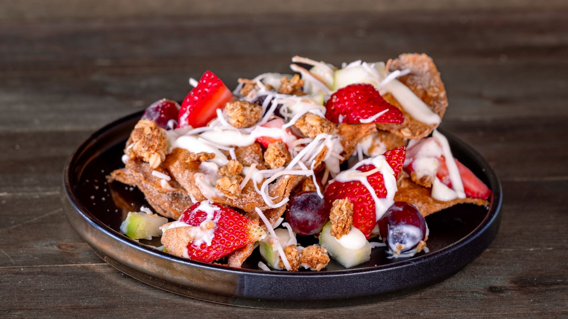 A plate of granola with strawberries, grapes, and fruit topped with yogurt from the 2025 menu at Disney California Adventure.