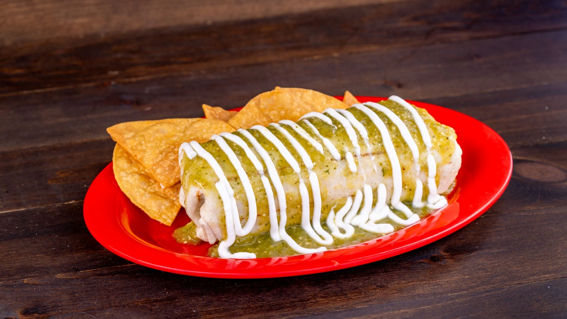 A 2025 Menu burrito with green sauce and sour cream, served with tortilla chips at Plaza de la Familia.