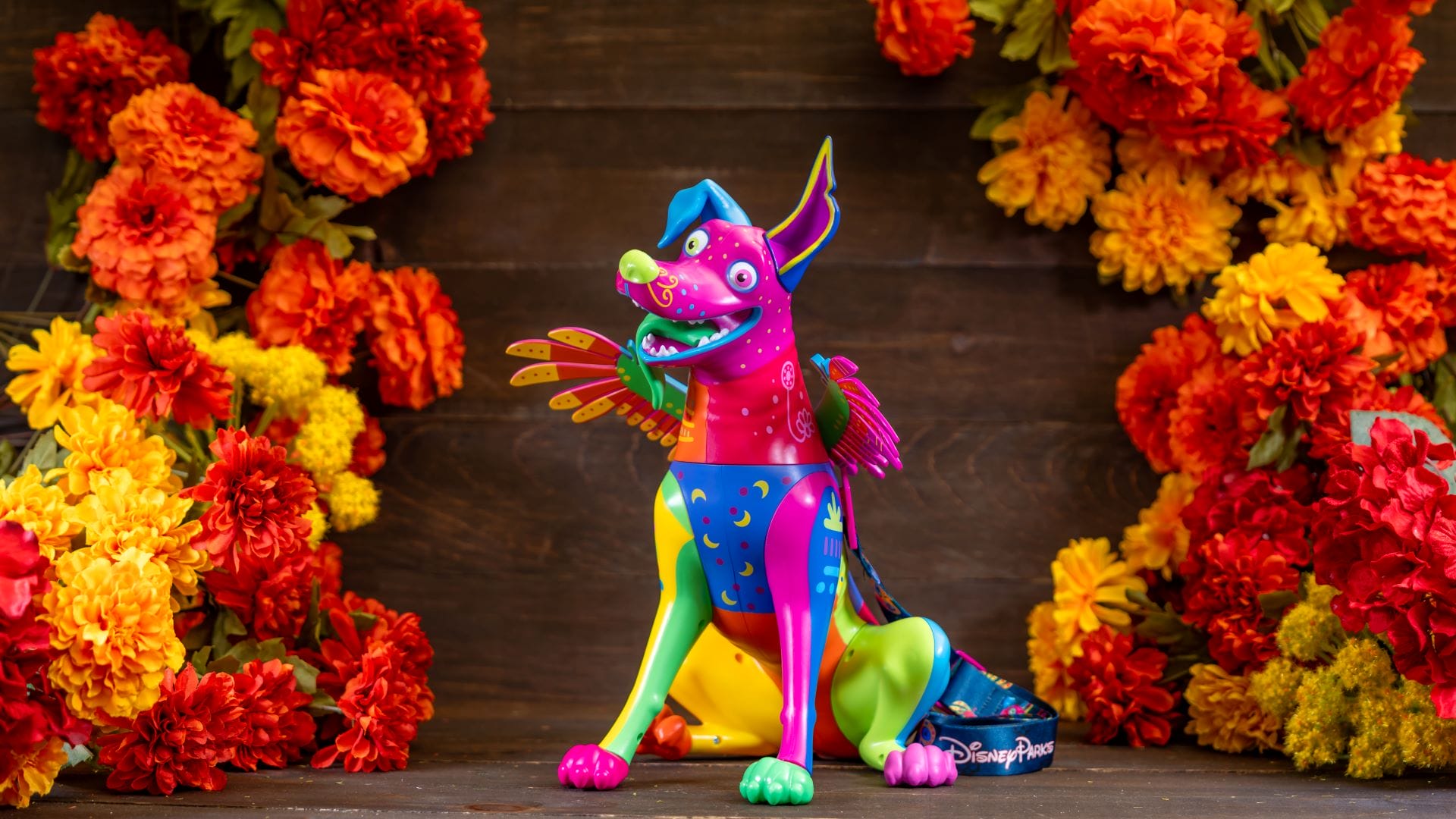 A colorful, winged dog figurine sits among vibrant marigolds at Plaza de la Familia in Disneyland Resort.