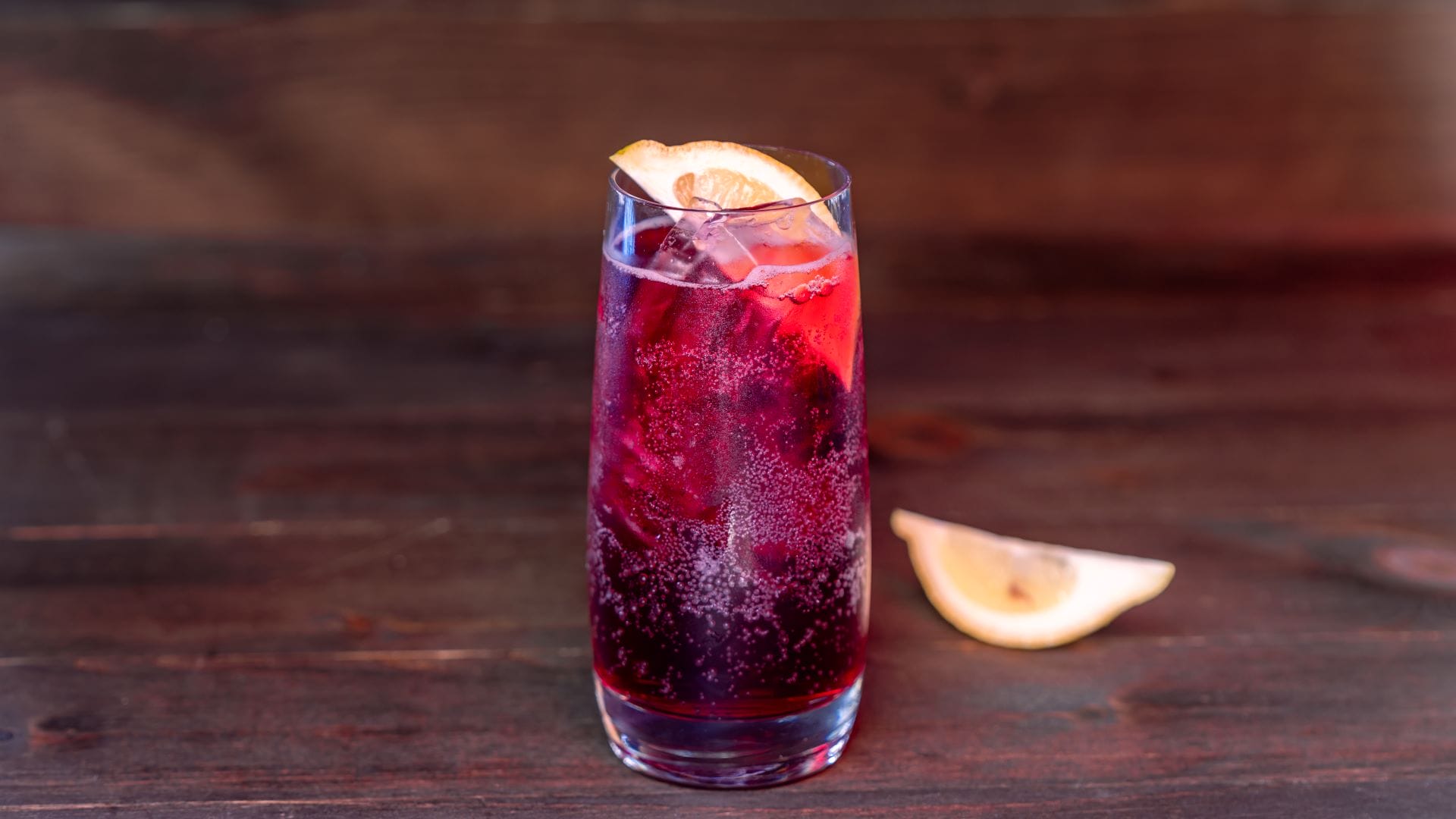 A tall glass of red fizzy drink with ice and lemon, inspired by the 2025 Plaza de la Familia menu at Disney California Adventure.