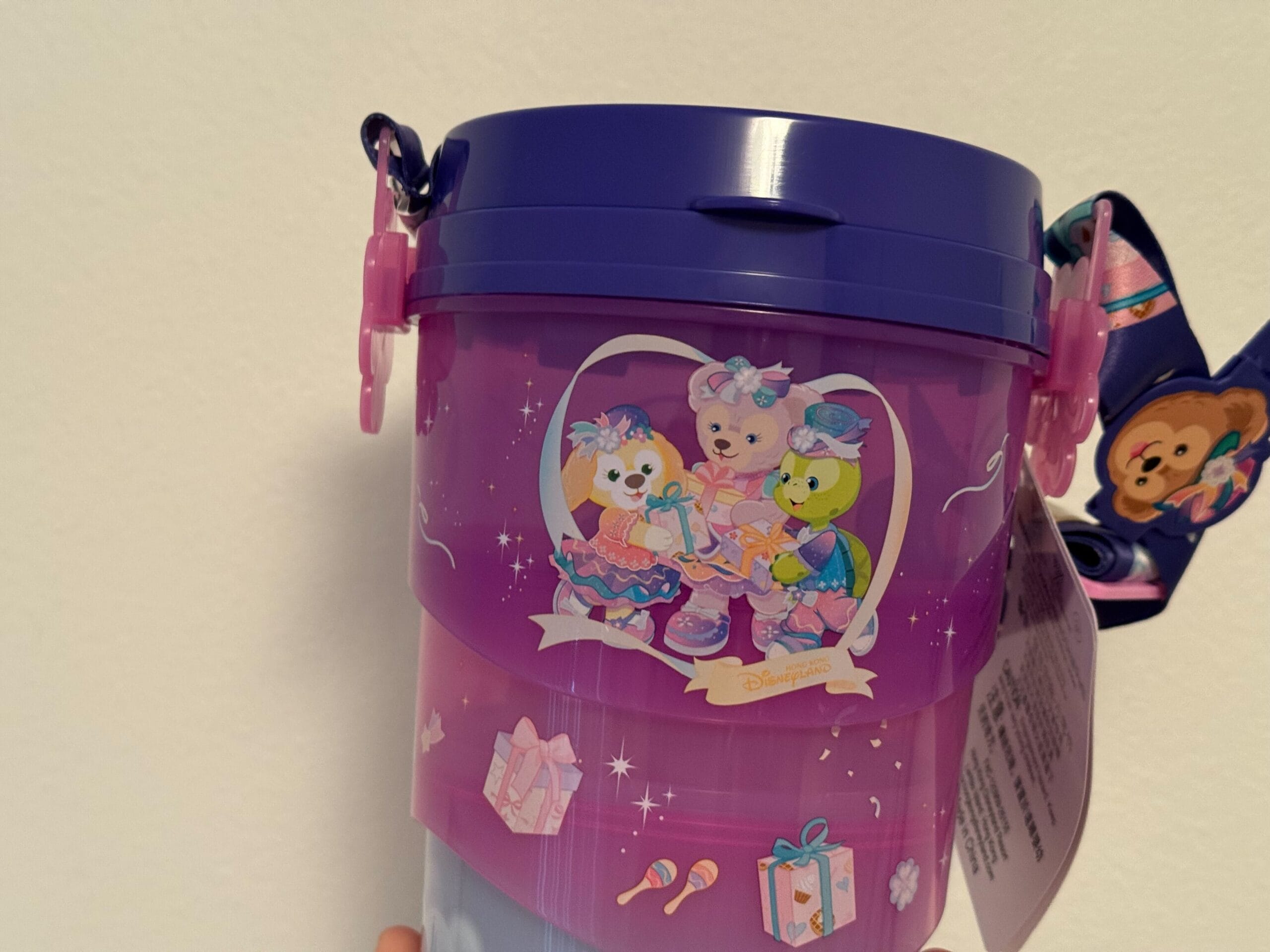Purple cup with three cartoon bears in fancy outfits, surrounded by gifts and party items, and a decorative strap attached.