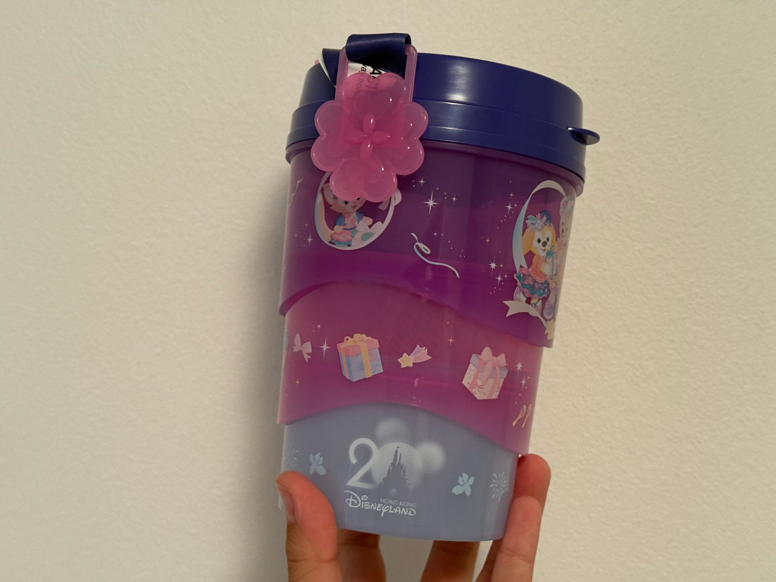 A purple Disneyland popcorn bucket with cartoon characters, a pink flower charm, and gift box designs.