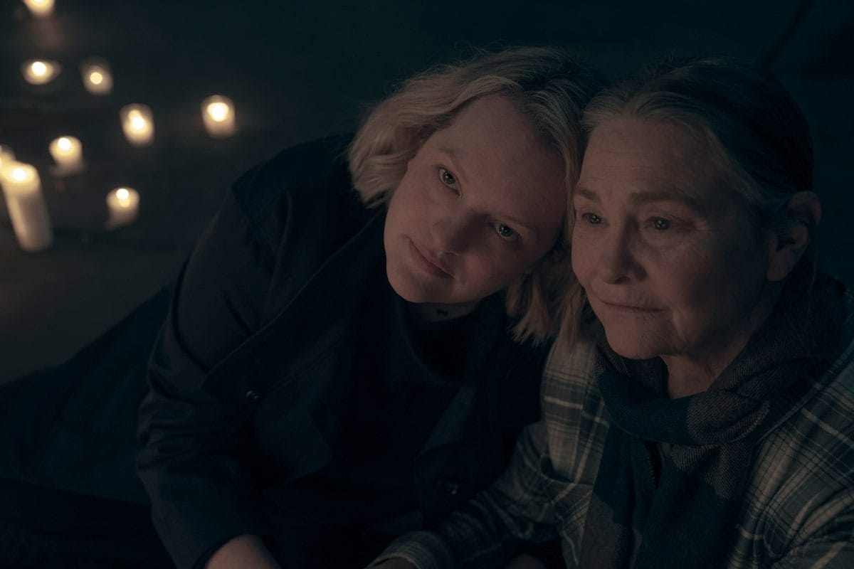 Two women sit close together in dim lighting, surrounded by Emmy Award-worthy candlelight, looking thoughtful and serene.