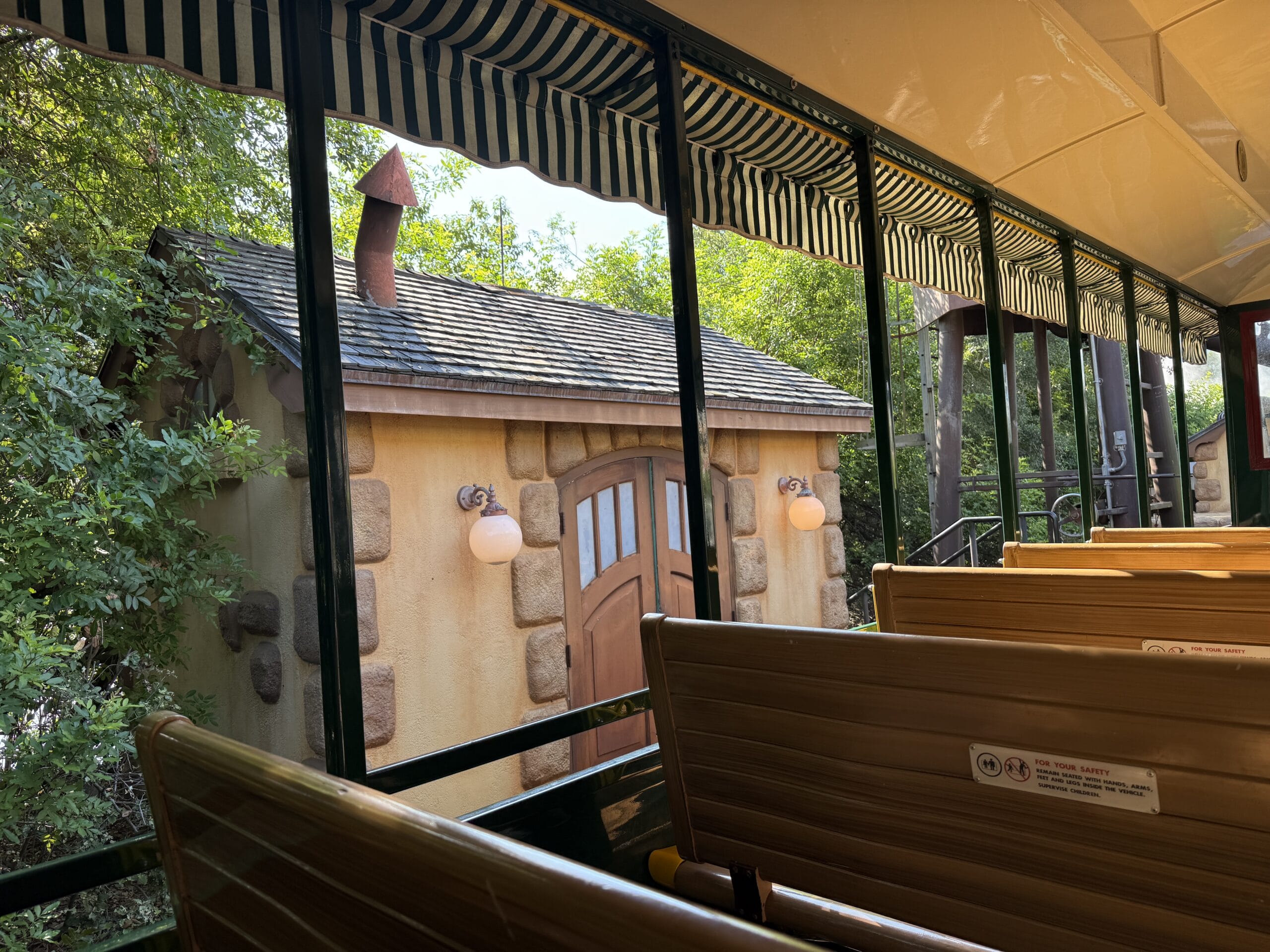 View from a tram with brown seats, looking at Frontierland Station on the Walt Disney World Railroad, surrounded by trees.