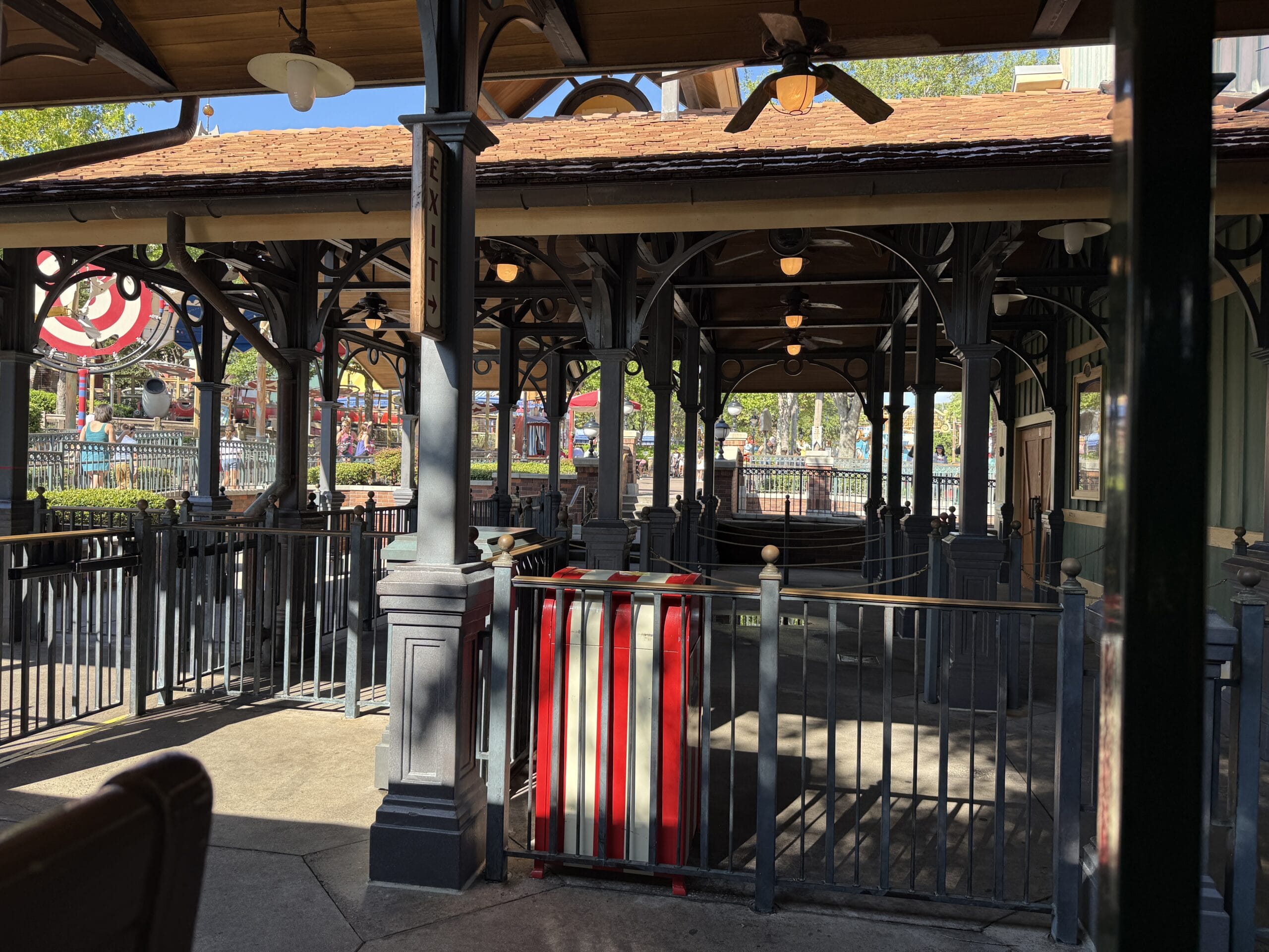 Empty Frontierland Station queue area with metal railings, wooden roof, and sunlight—part of the Walt Disney World Railroad loop.
