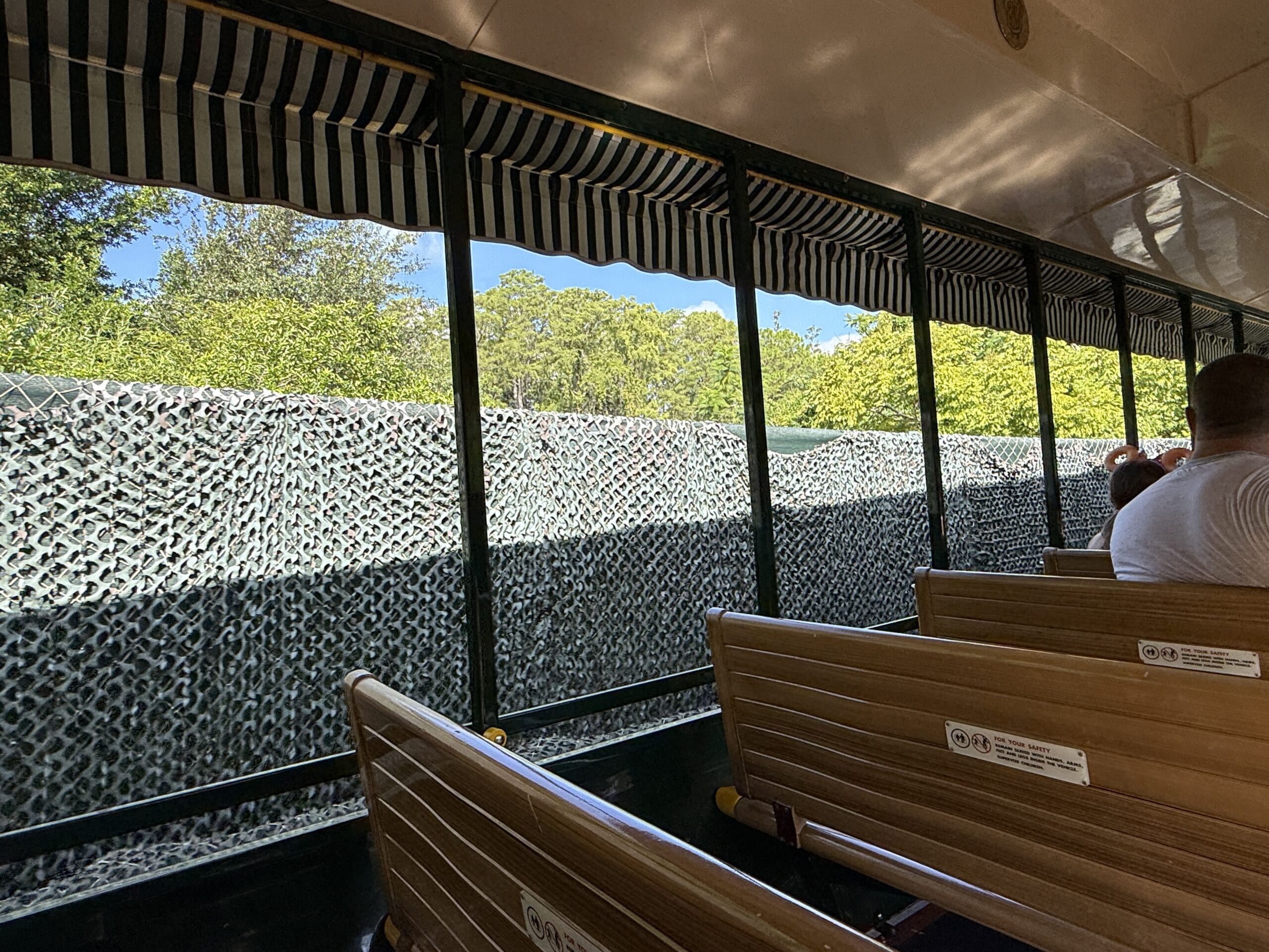 People sit on a tram with wooden benches, passing Frontierland Station near the Walt Disney World Railroad's complete loop.