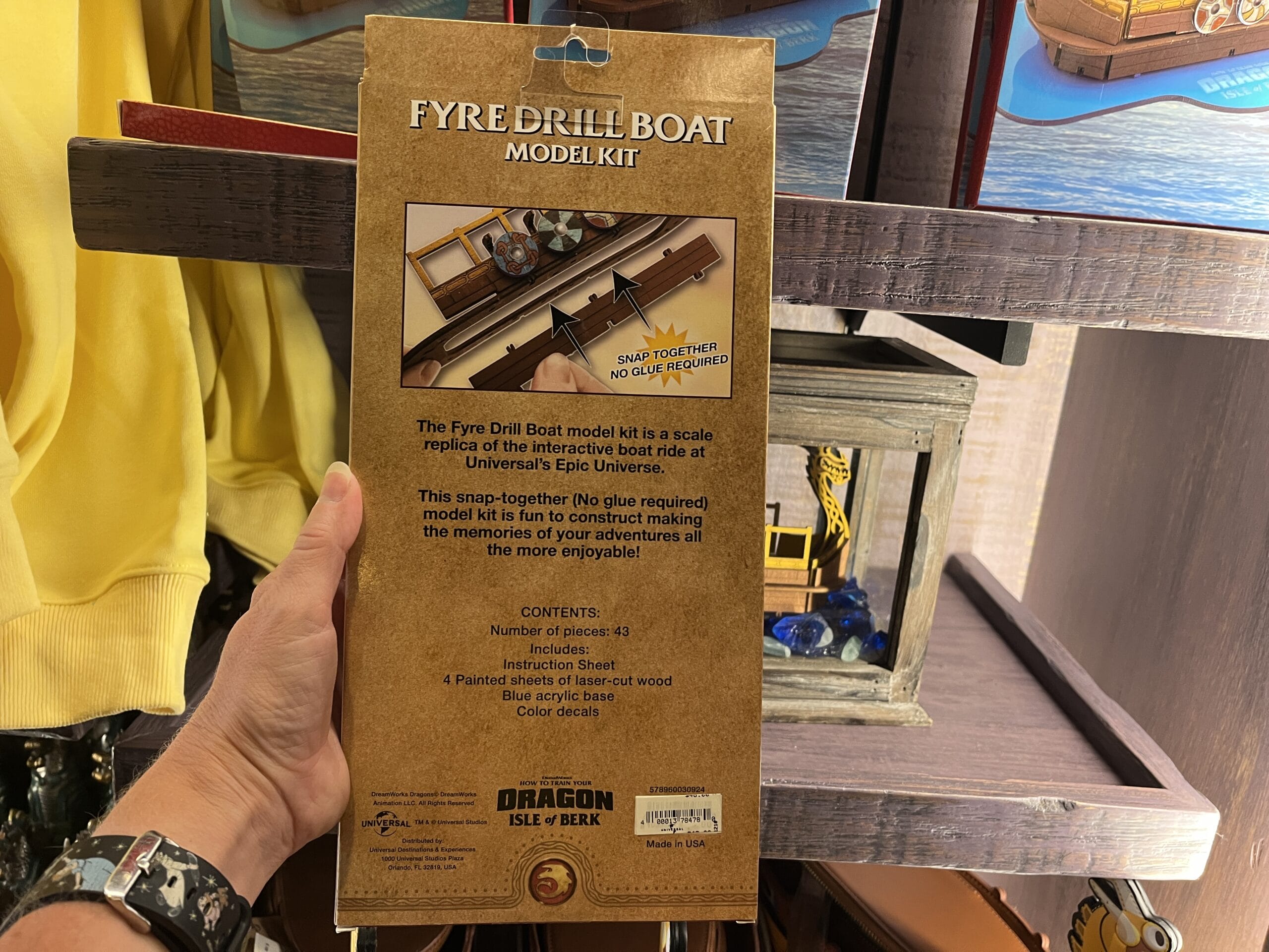 A hand holds a "Fyre Drill Boat Model Kit" box from Hiccup's Work Shop, showing instructions and contents on the back.