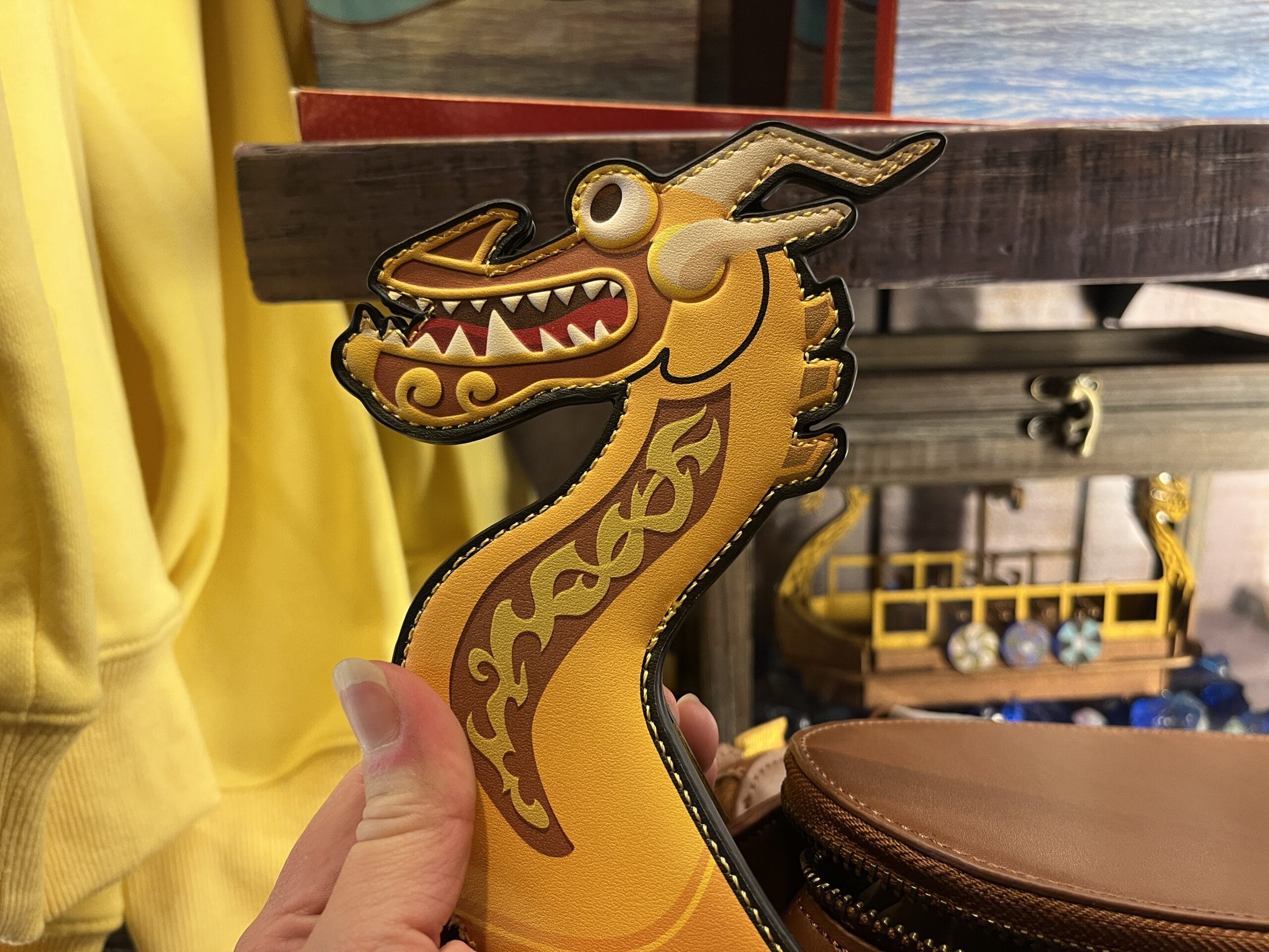 A hand holds a cartoonish yellow dragon from Hiccup's Work Shop, grinning with decorative swirls on its neck.
