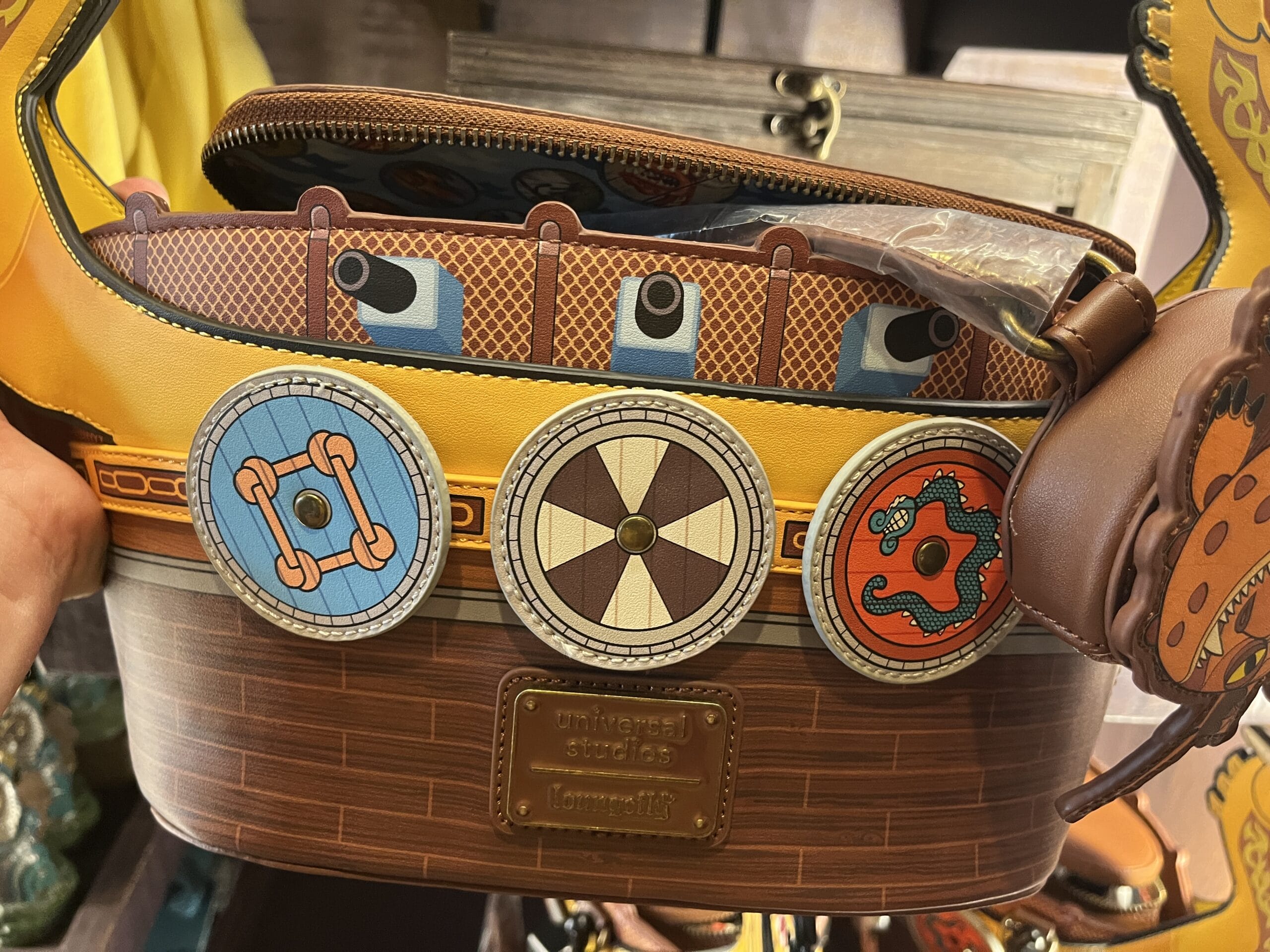 A brown Universal Studios bag from Hiccup's Work Shop, designed like a Viking ship with colorful shields and dragon details.