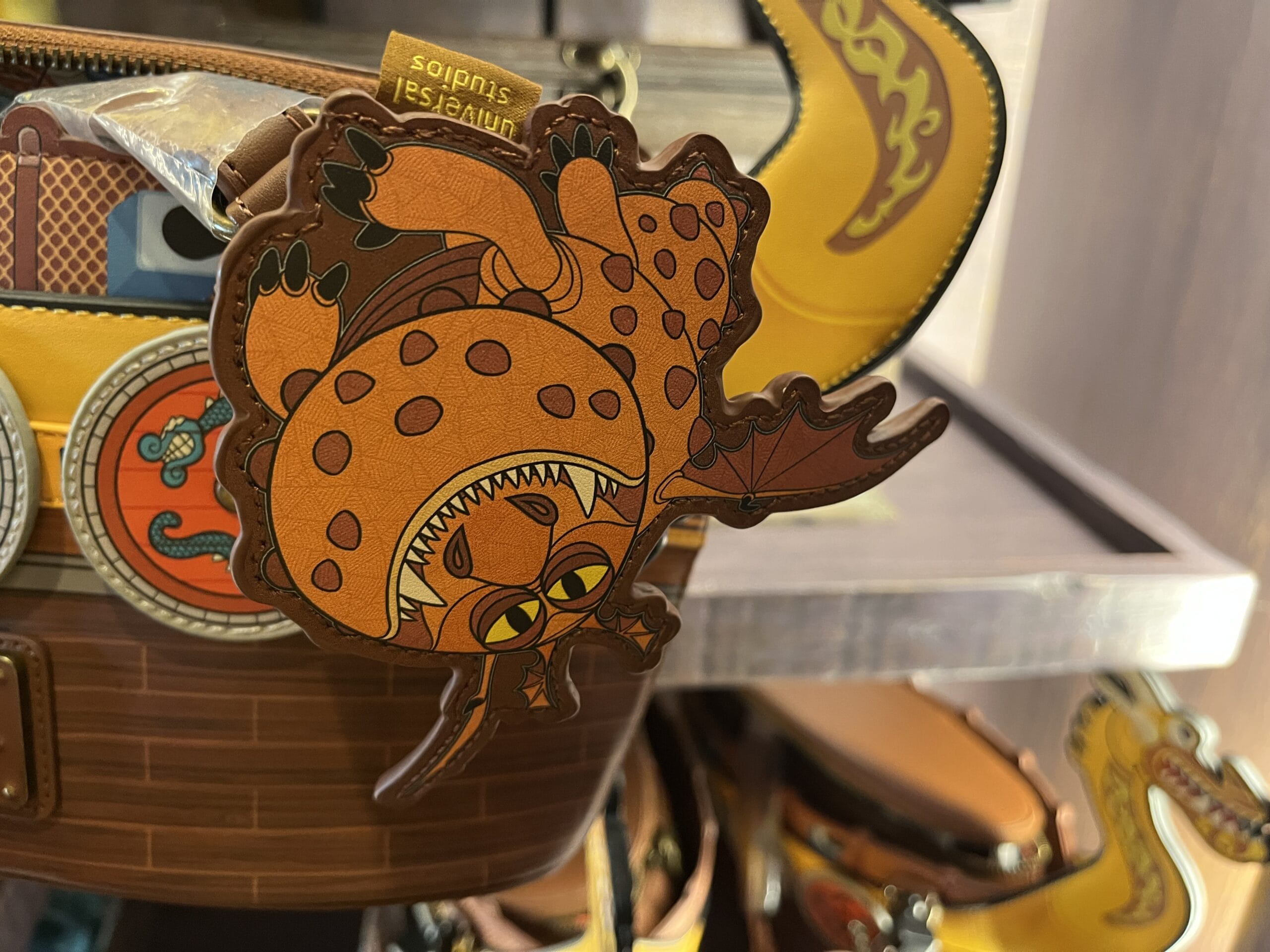 A cartoon orange dragon keychain from Hiccup's Work Shop hangs from a wooden ship-themed bag.
