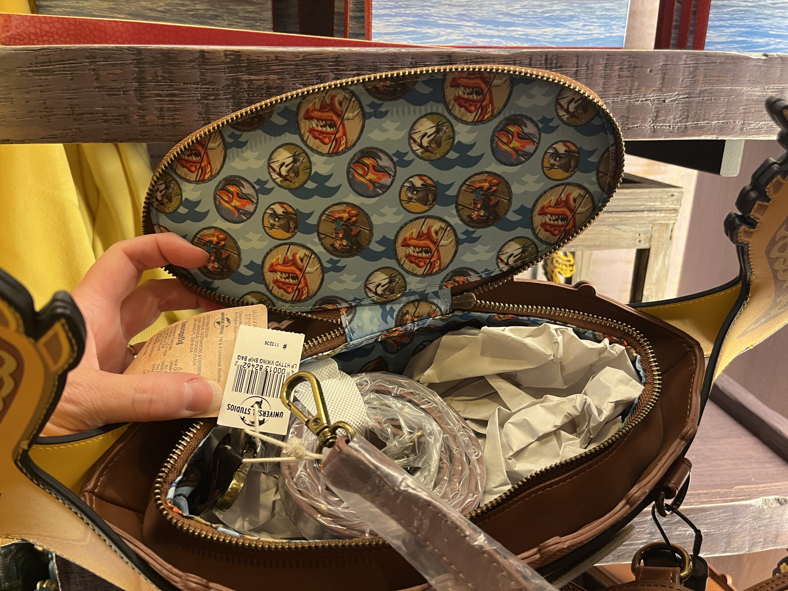 A hand opens a Hiccup's Work Shop bag, revealing a colorful shark-mouth interior and bundled strap inside.