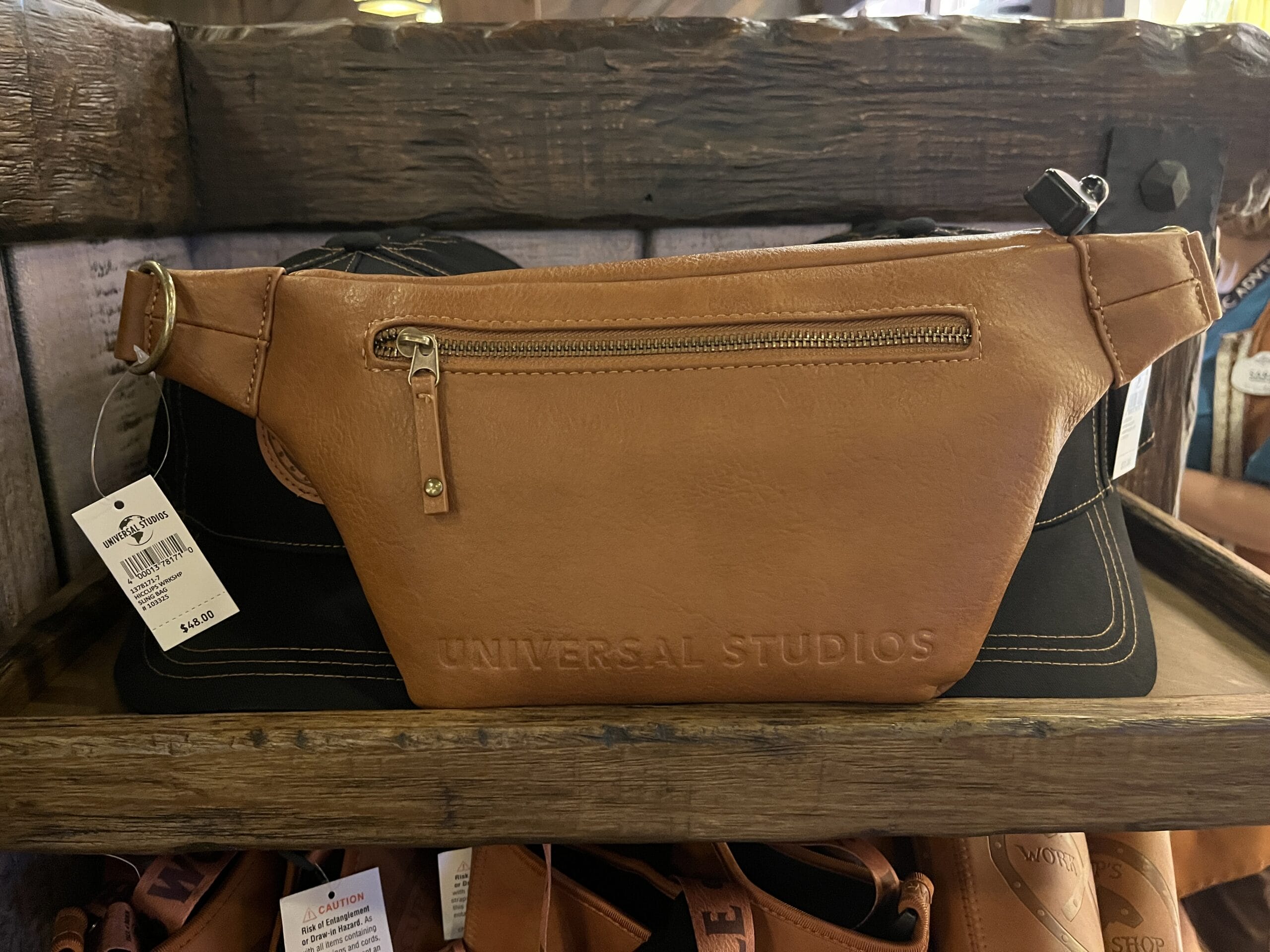 A brown leather fanny pack from Hiccup's Work Shop with "Universal Studios" embossed, displayed on a wooden shelf.