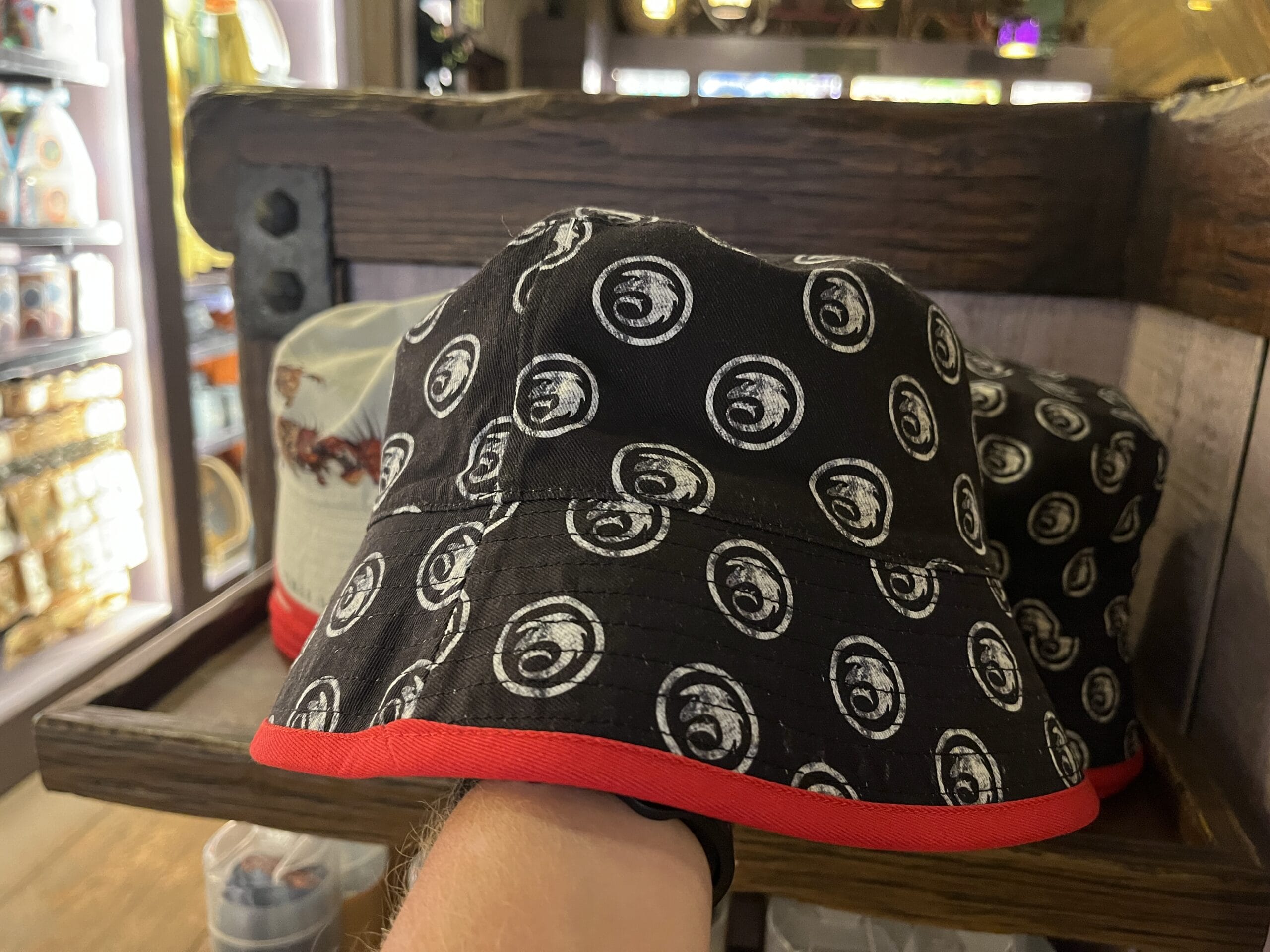 A black bucket hat with white spiral snake designs and a red brim is showcased at Hiccup's Work Shop.