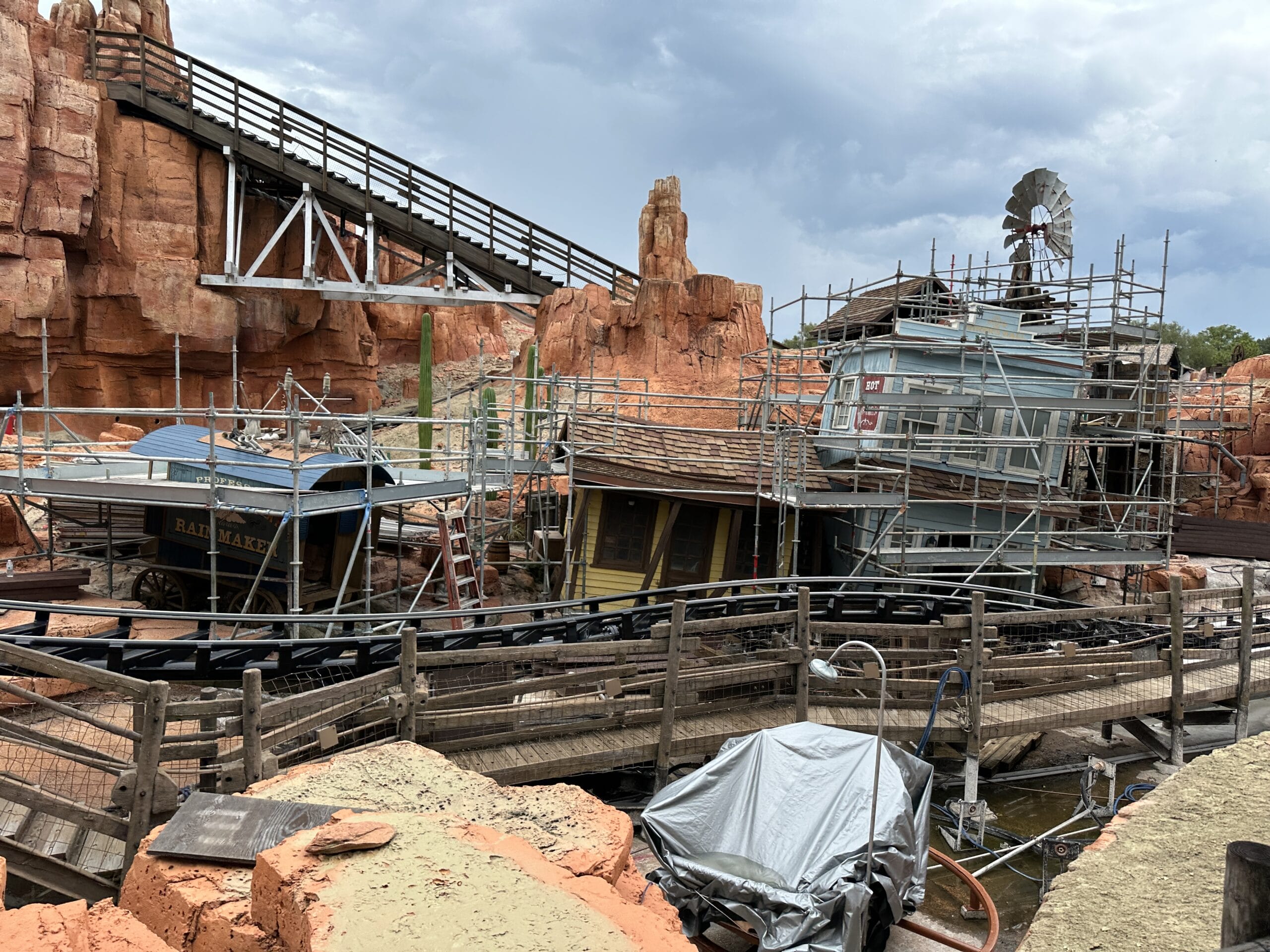 Wooden buildings under construction with scaffolding, near red rocks and the Walt Disney World Railroad track.