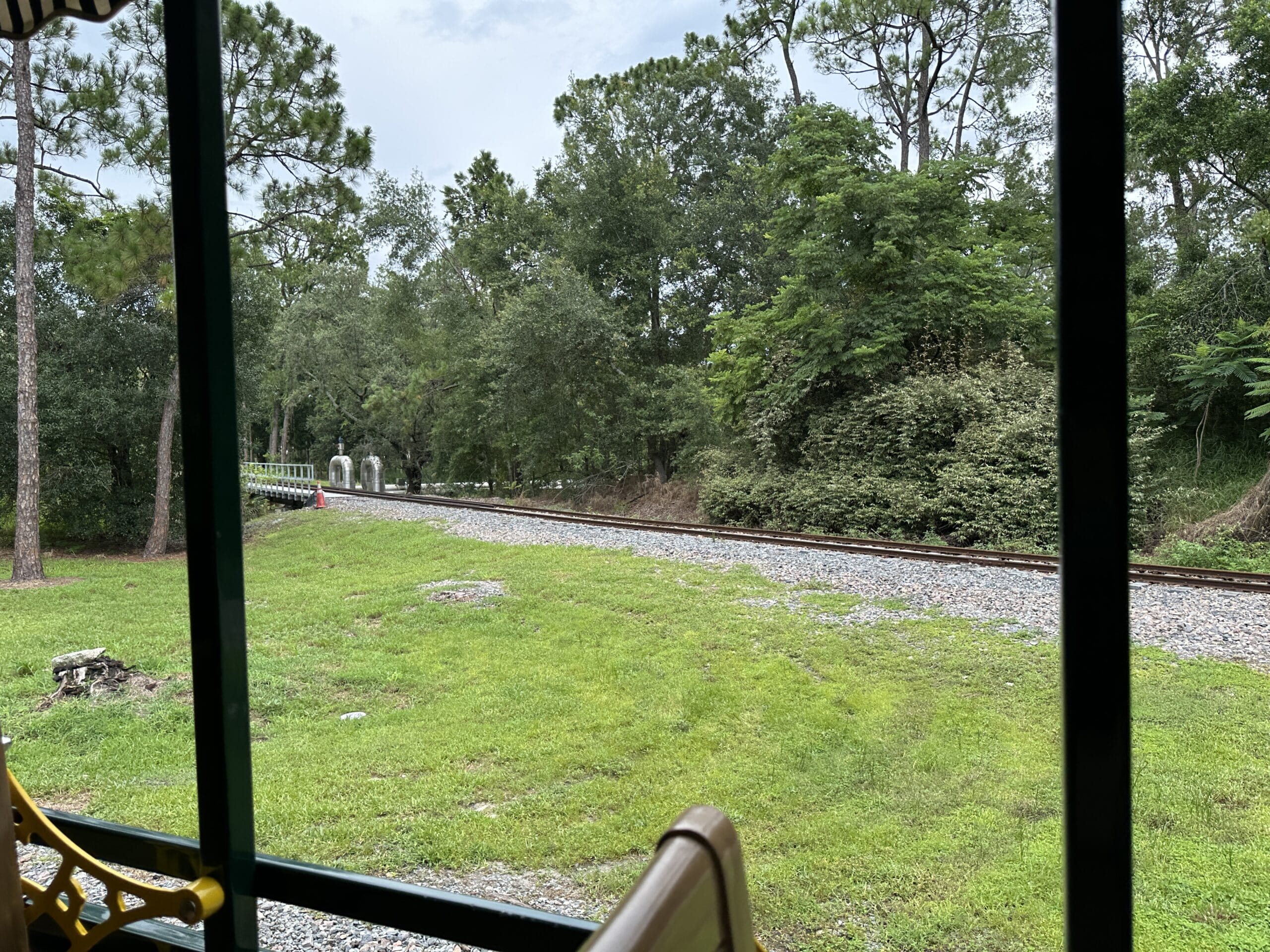 View from the Walt Disney World Railroad as it nears Frontierland Station, with tracks curving through green grass and trees.