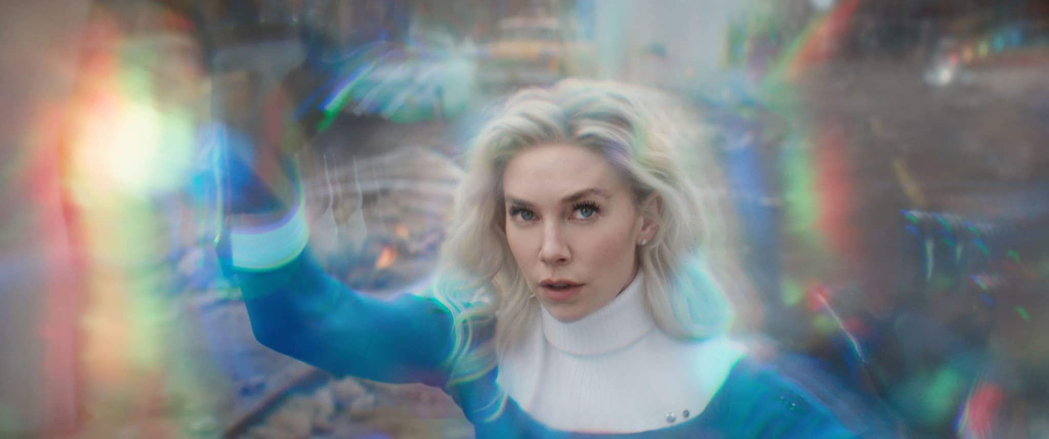 A woman with blonde hair raises her hand, surrounded by glowing energy like a Fantastic Four scene.