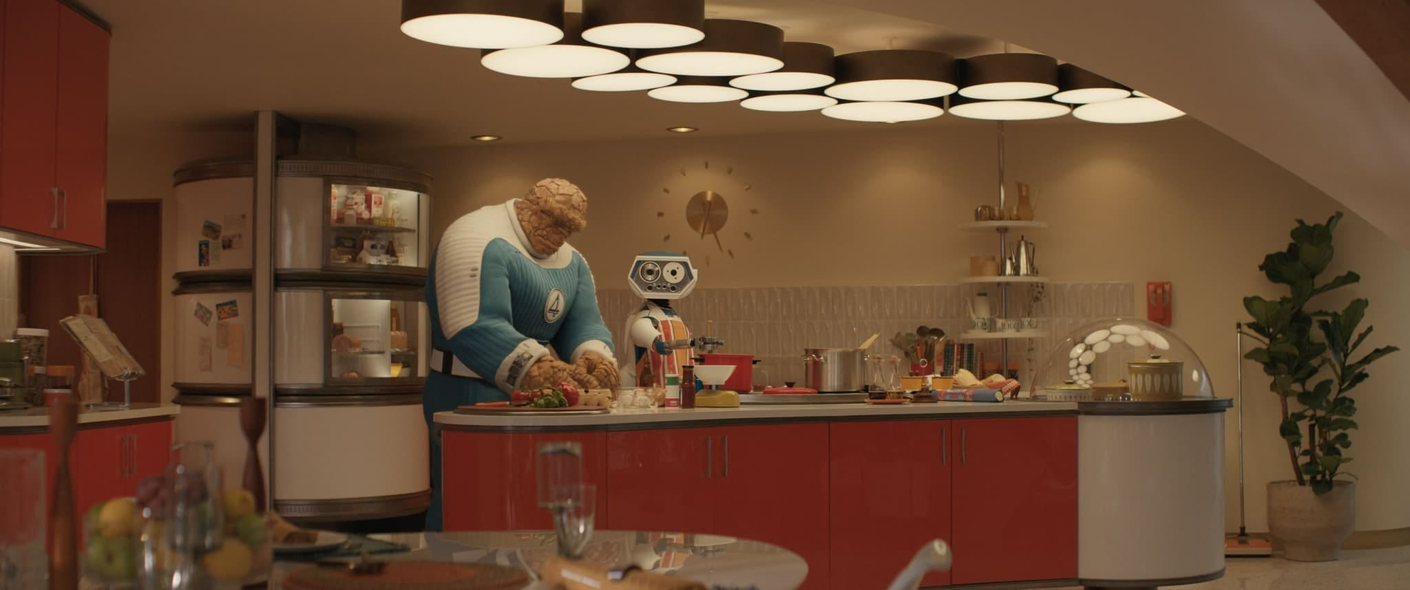 A large rock-like figure and a small robot cook in a Fantastic Four-themed kitchen with retro red cabinets.