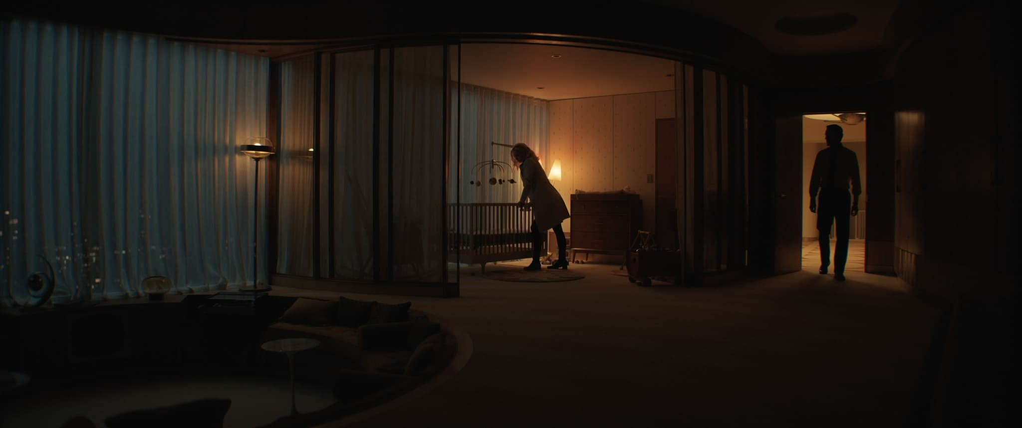 A woman leans over a crib in a dim room as Reed Richards stands in the doorway, both figures in silhouette.