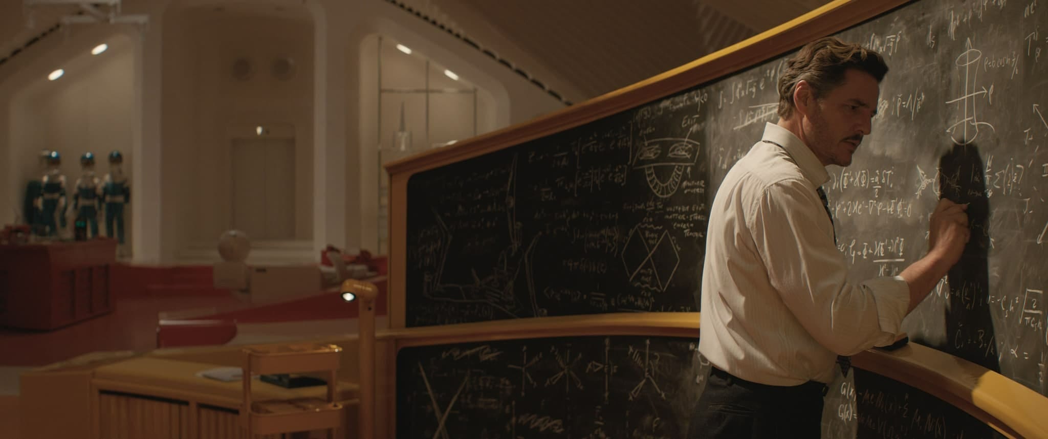 Reed Richards writes equations on a large chalkboard in a futuristic, dimly lit room with white and red decor.