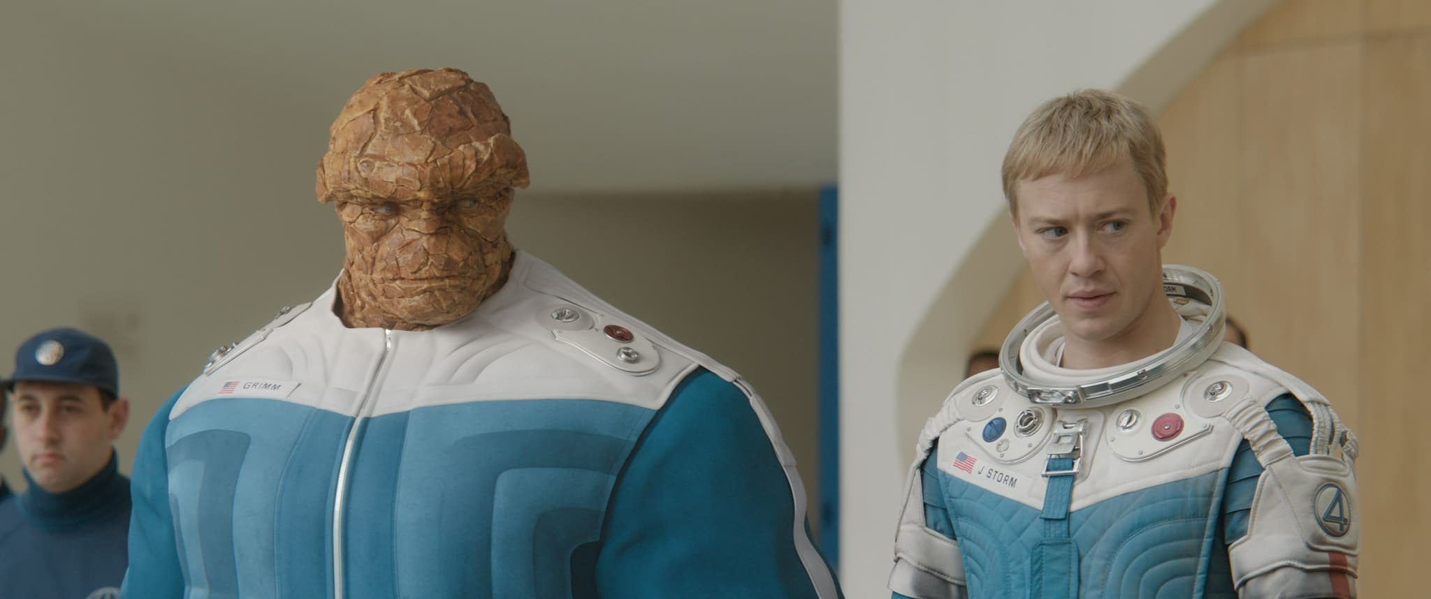 A Fantastic Four member in blue and white gear stands beside a rock-like ally, capturing their First Steps indoors.