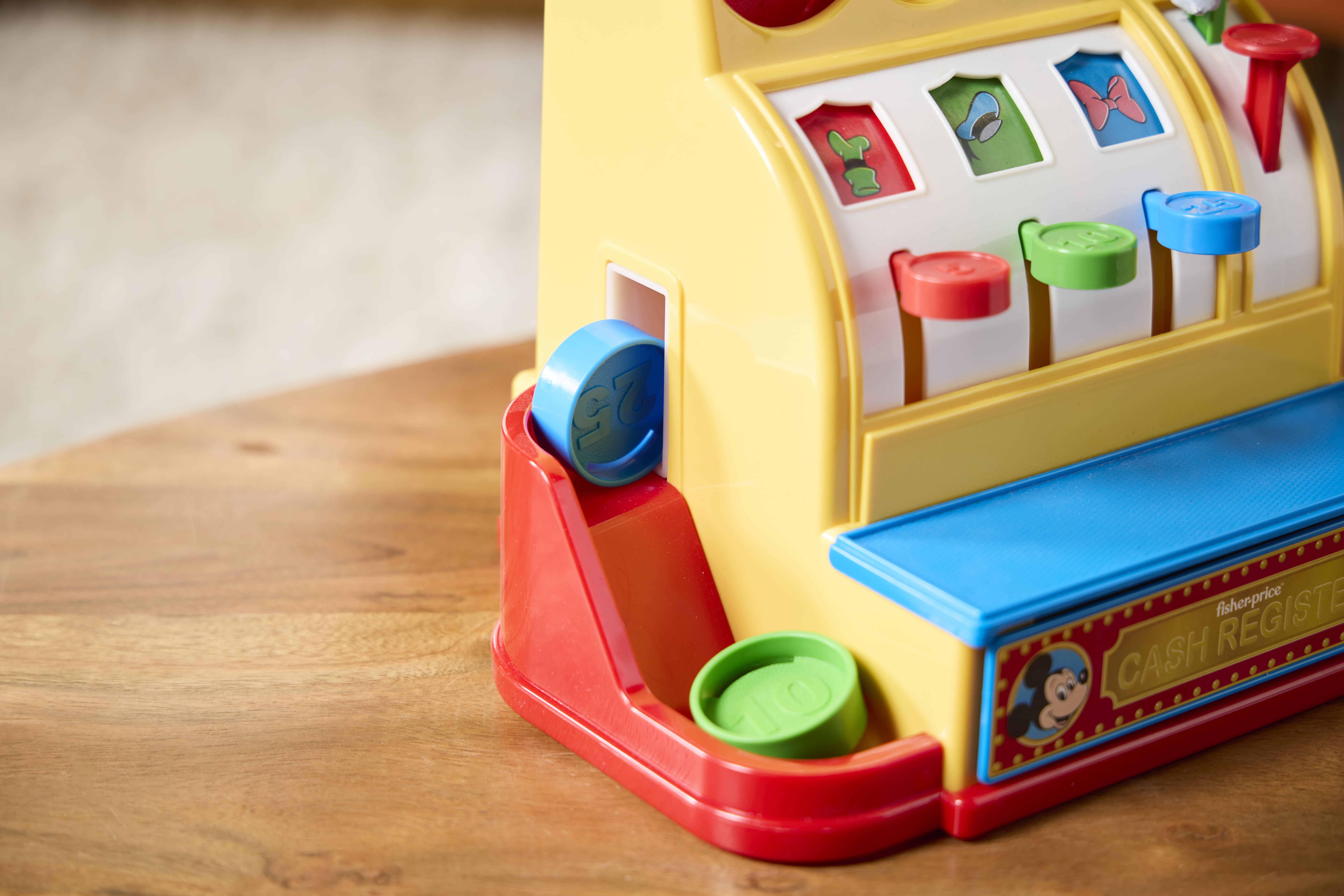Close-up of a colorful toy cash register with plastic coins, inspired by Retro Fisher Price toys, on a wooden table.