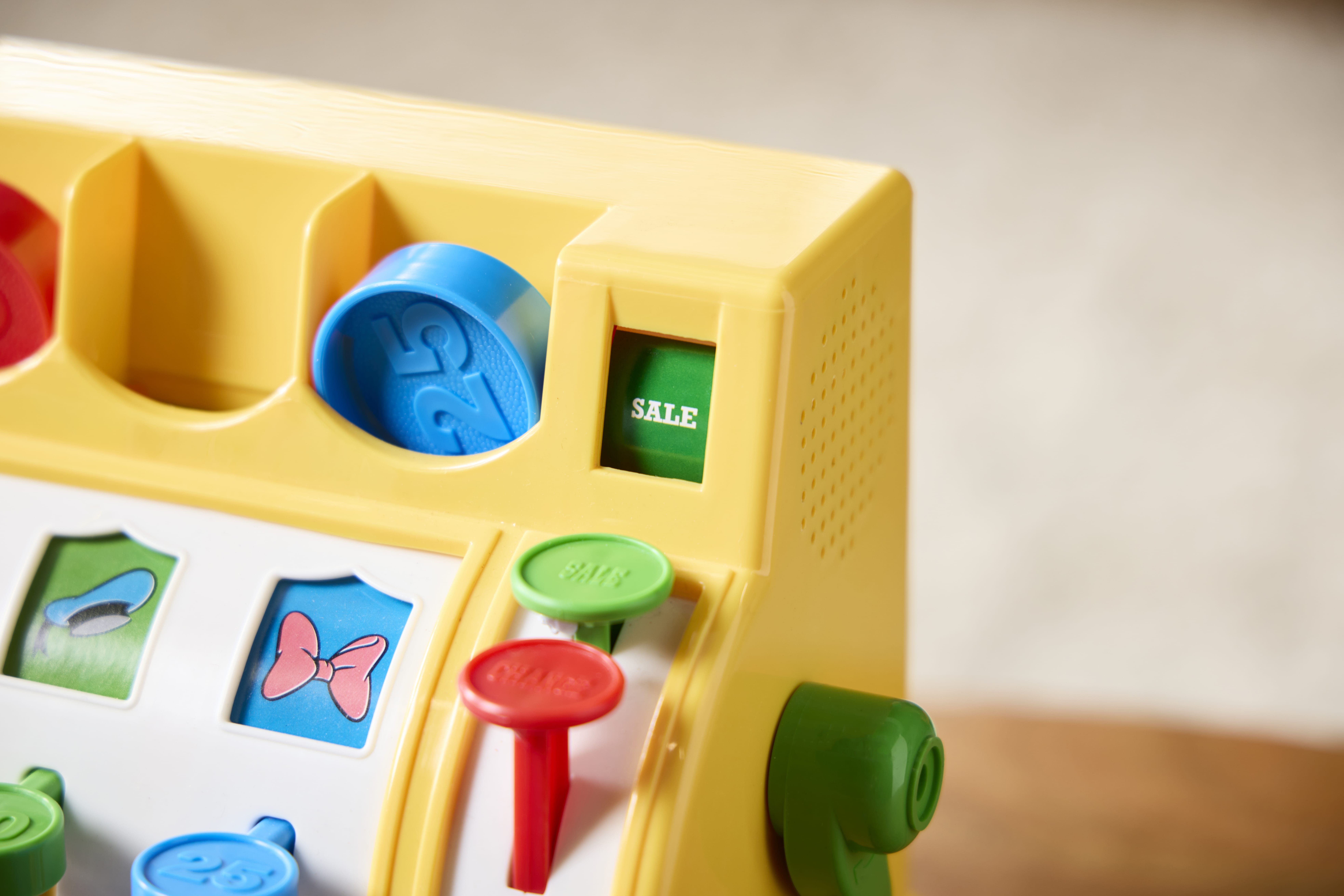 Close-up of a yellow retro Fisher Price toy cash register with colorful buttons and a green "SALE" button.