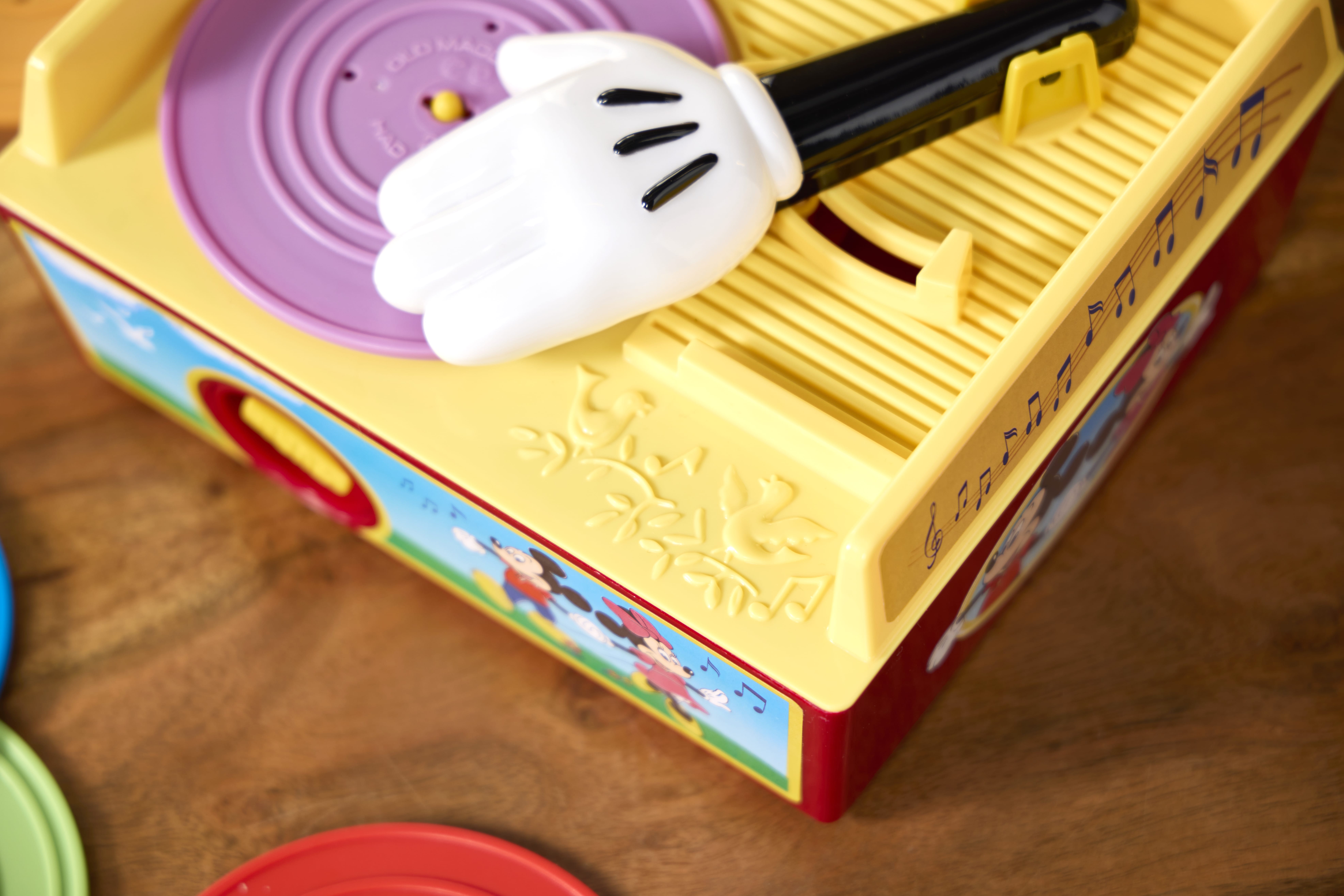 A colorful toy music box with a cartoon glove arm, inspired by retro Fisher Price toys, sits on a wooden surface.