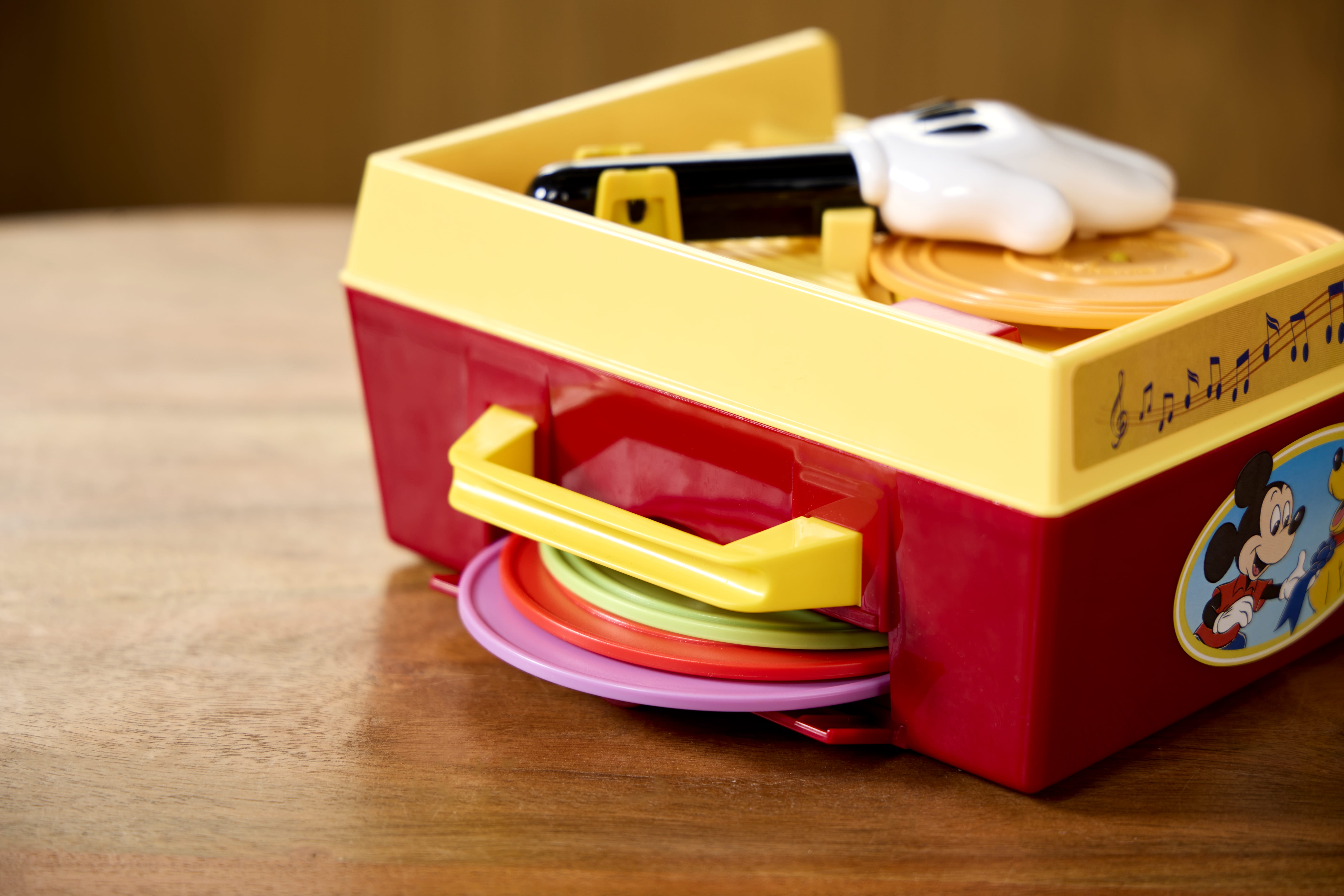 A retro Fisher Price toy record player with a Mickey Mouse sticker sits on a wooden table.