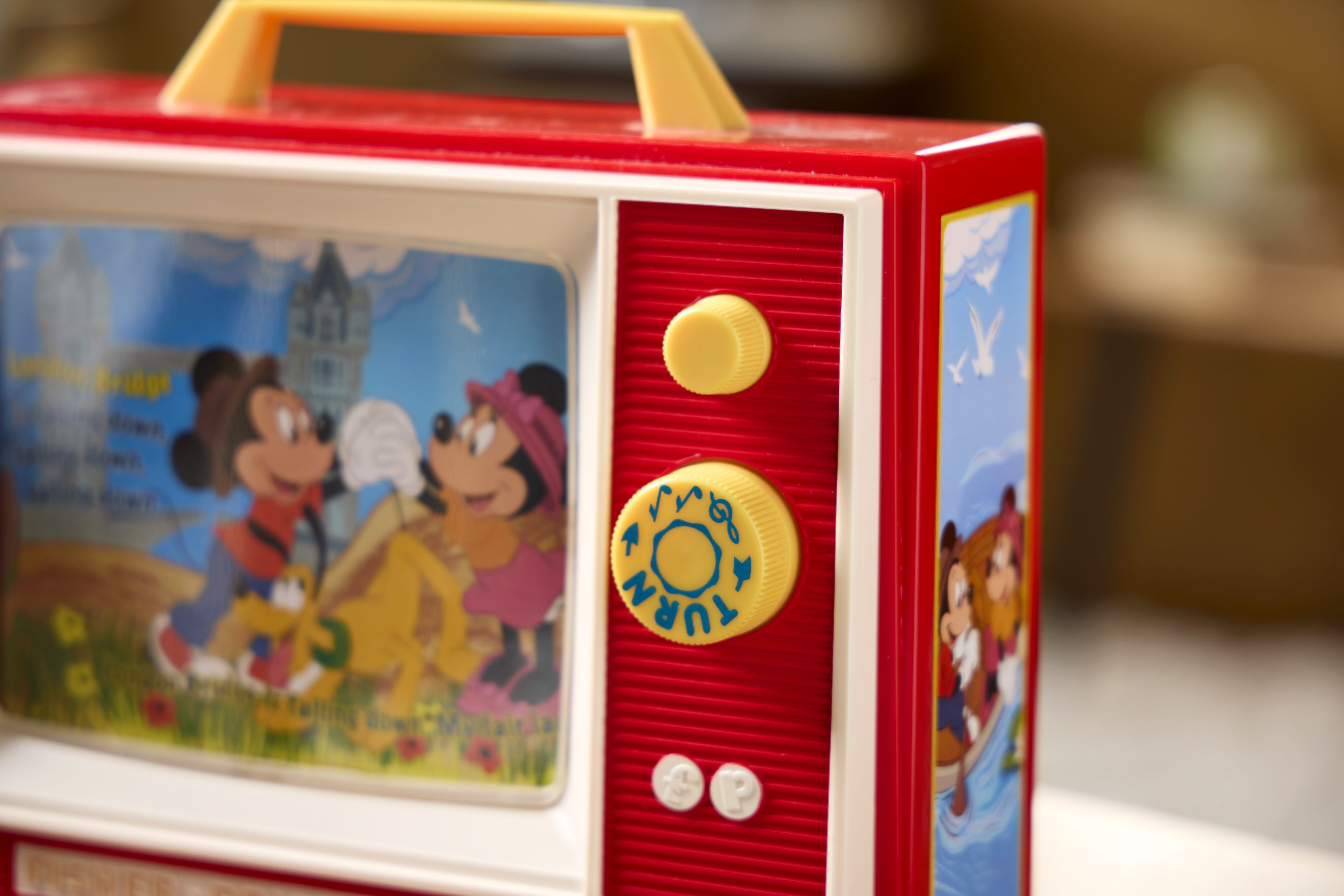 Close-up of a red retro Fisher Price toy TV with cartoon animals and a yellow turn knob on the side.