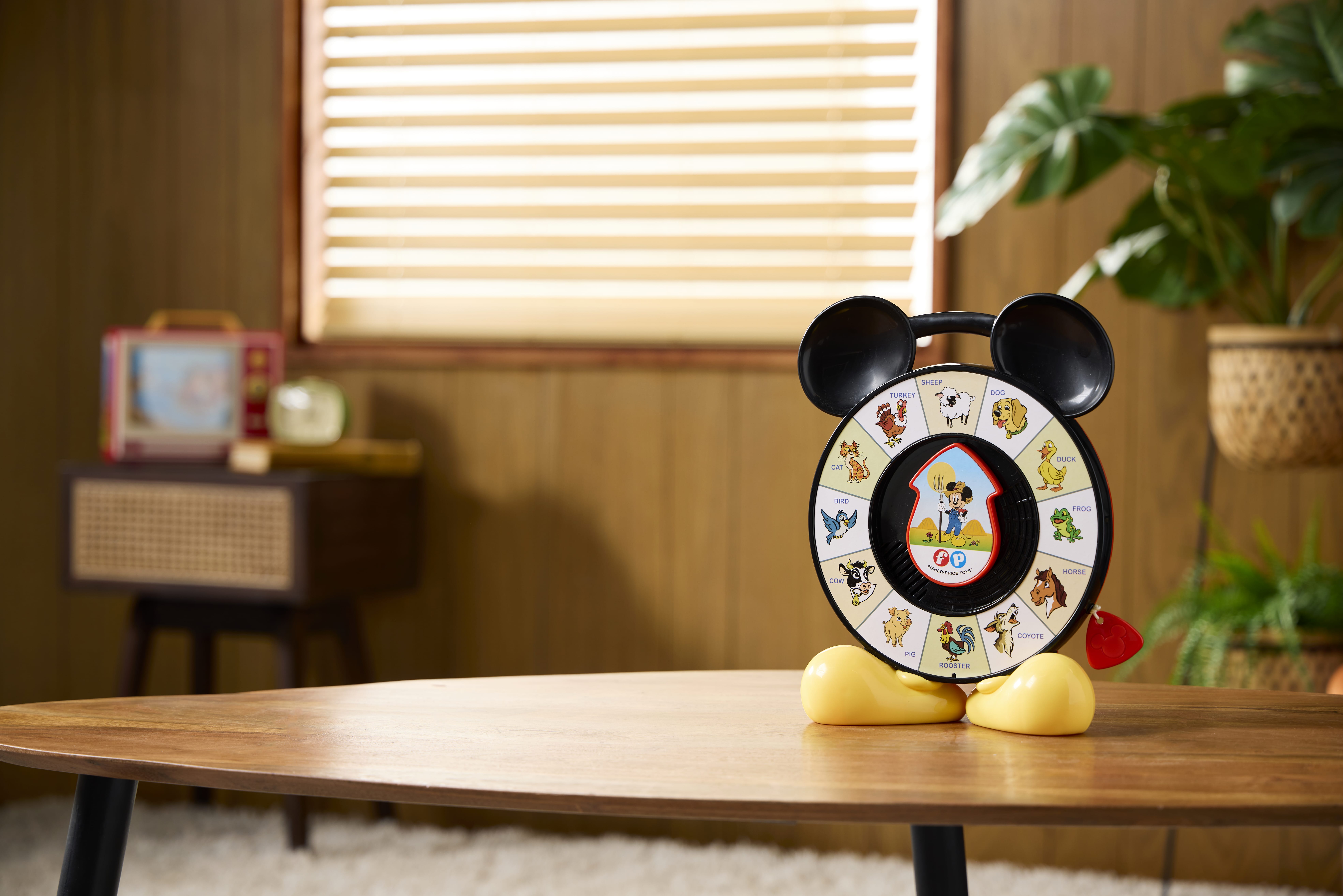 A vintage Mickey Mouse See ‘n Say, one of the classic Disney toys, sits on a wooden table in a cozy, retro-styled room.