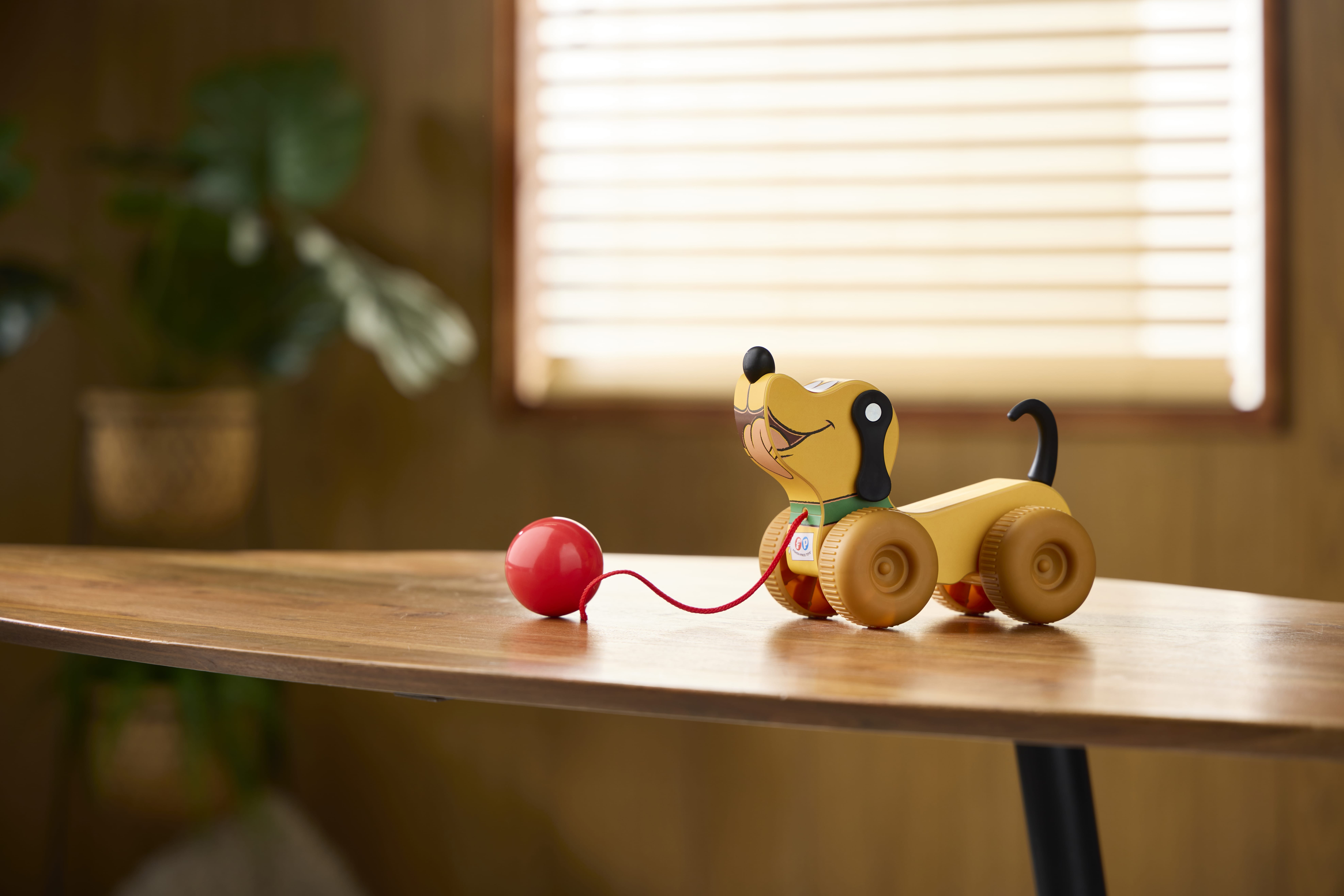 A Retro Fisher Price wooden dog with a red pull string sits on a table, sunlight streaming through blinds behind it.