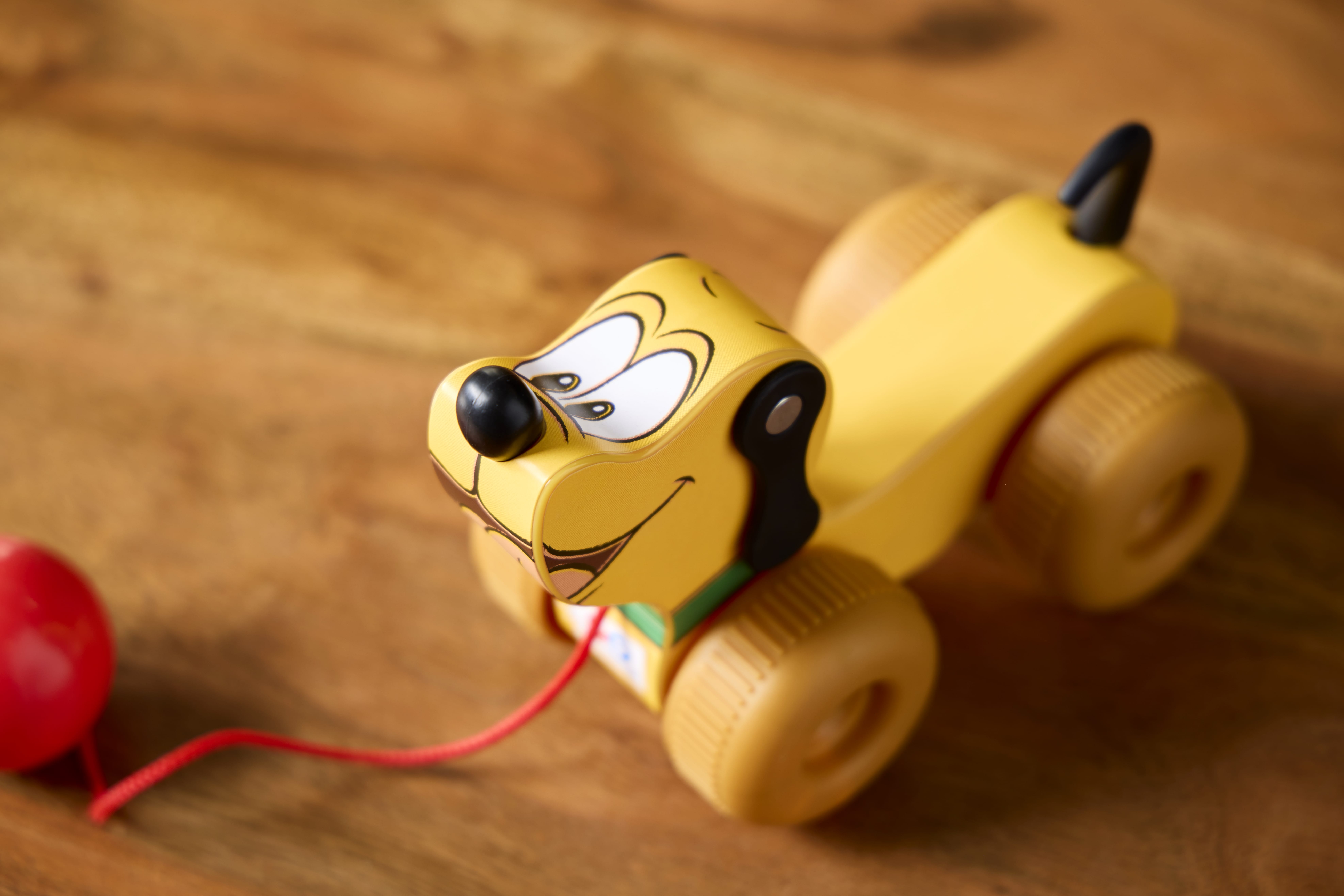 A yellow Retro Fisher Price toy dog on wheels with a red pull string, sitting on a wooden surface.