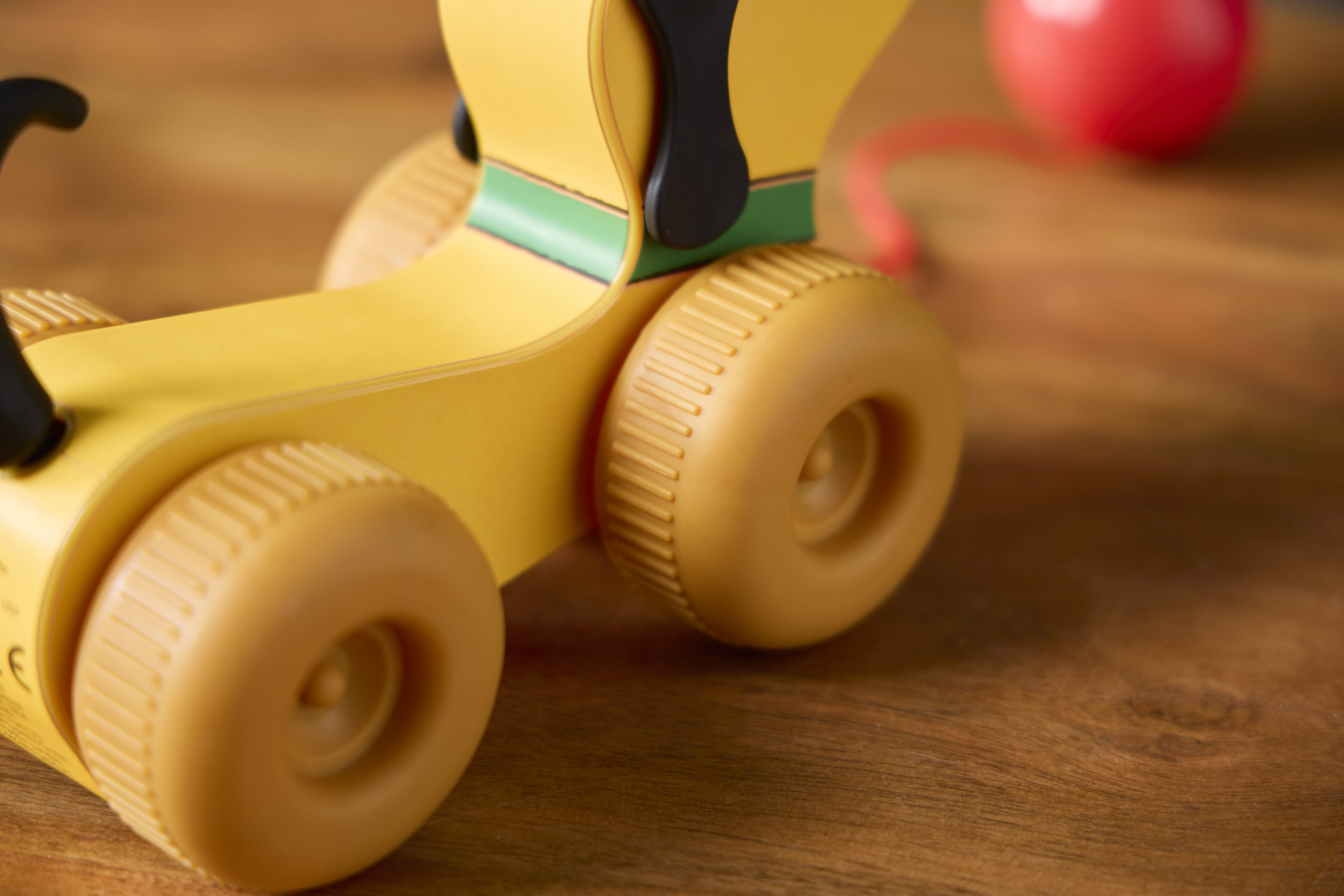 Close-up of a Retro Fisher Price yellow toy with large wheels on wood, red ball in the background. Available online.