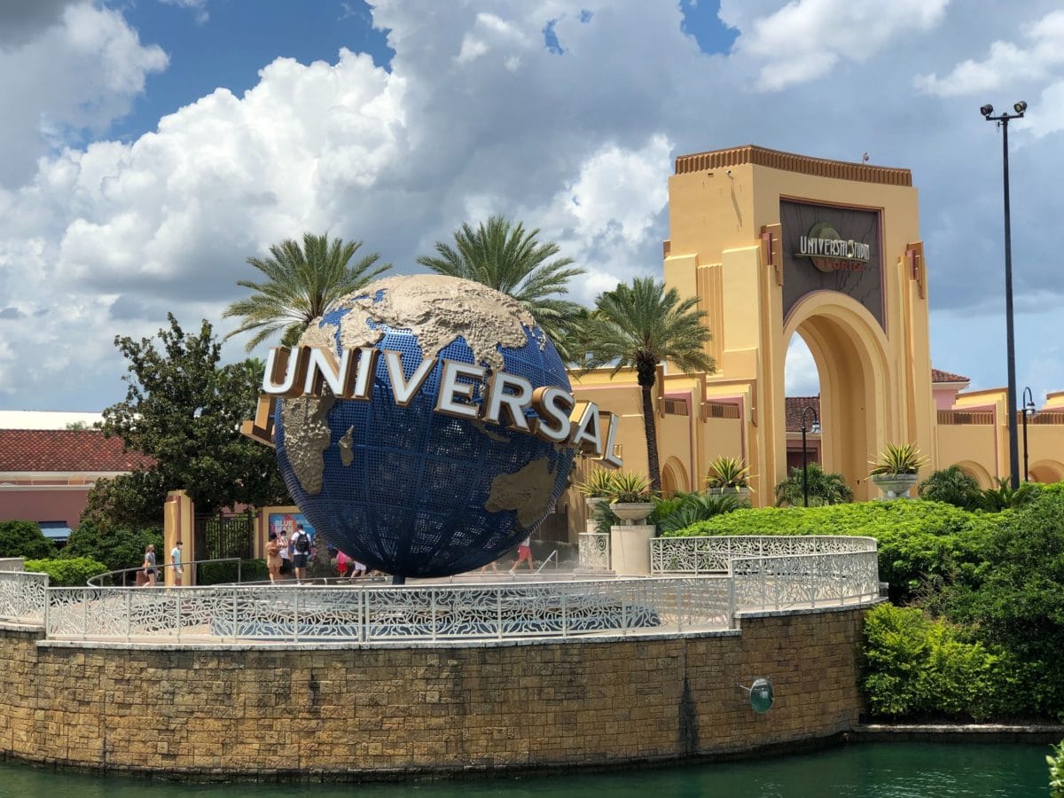The Universal Studios globe statue greets guests at Universal Orlando Resort, framed by palm trees and a blue sky.
