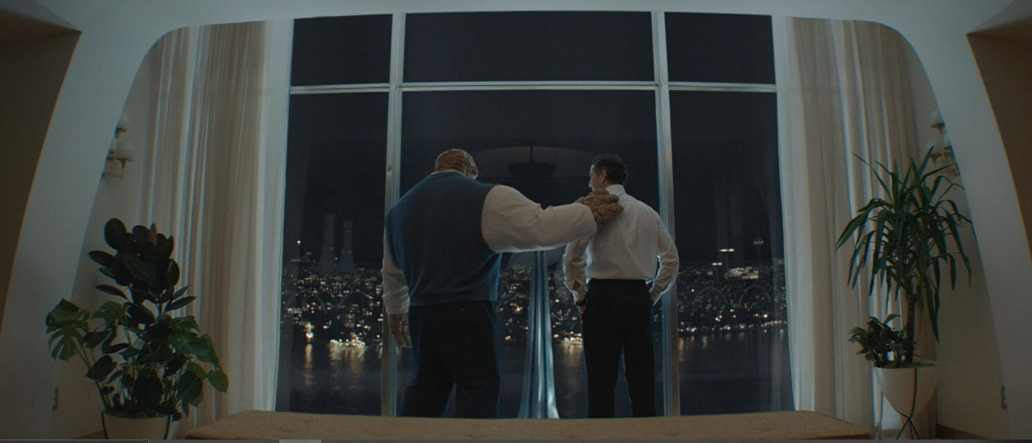 Two men in dress shirts stand by a large window at night, taking their first steps toward a fantastic city skyline view.