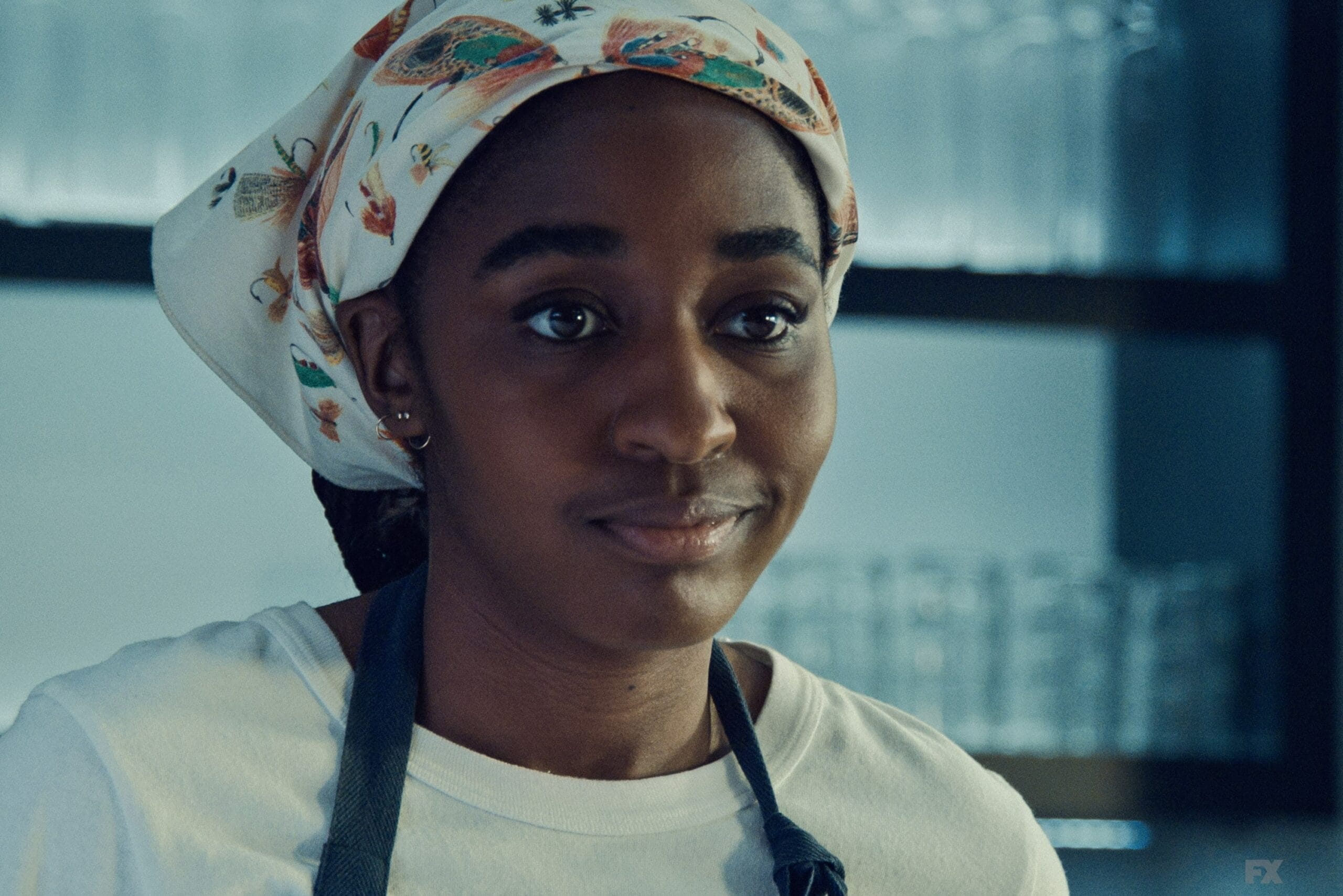 A woman in a headscarf and apron looks ahead calmly in a kitchen, inspired by the Walt Disney Company's creativity.