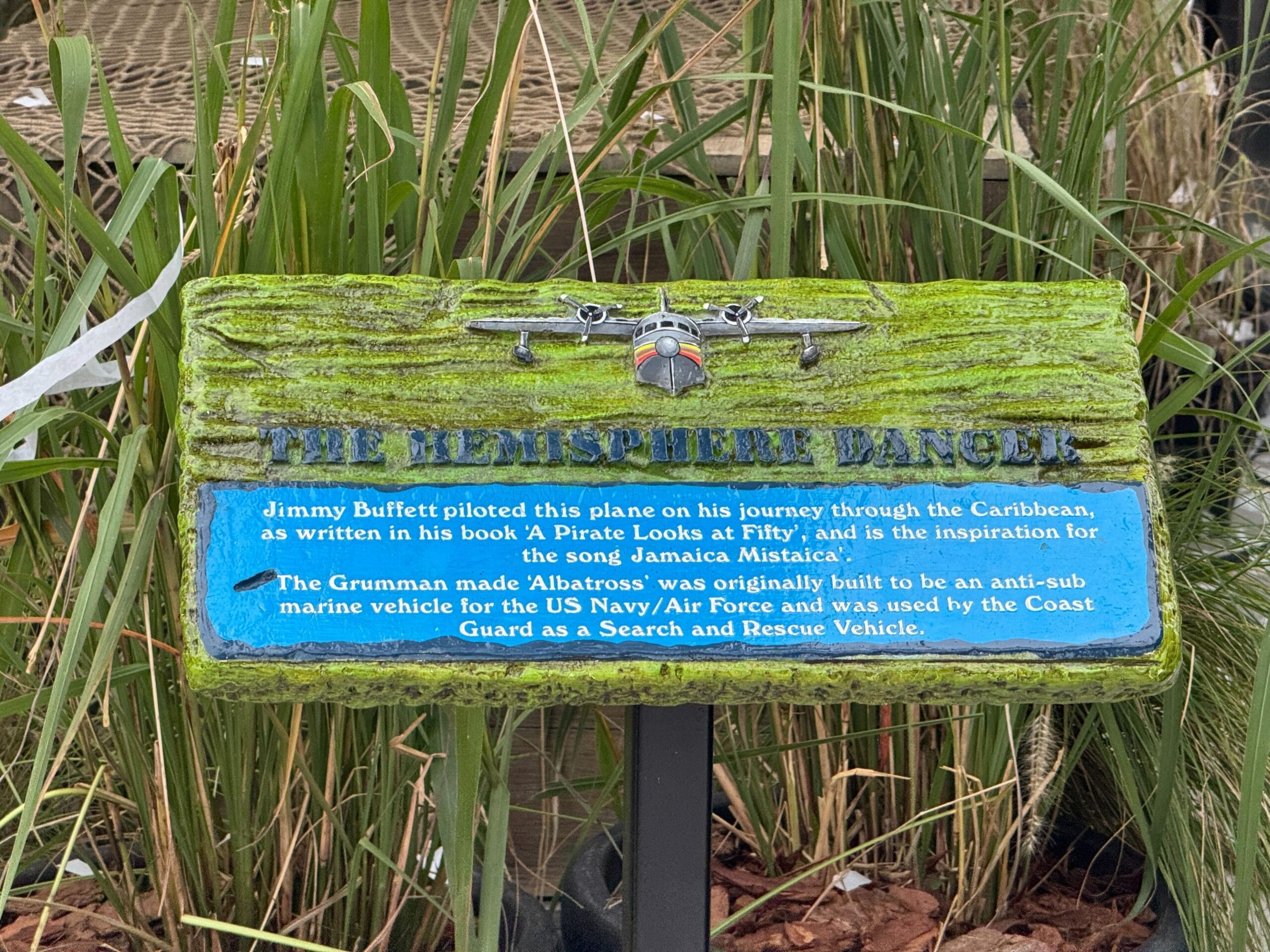 A mossy sign features the Hemisphere Dancer model plane, celebrating Jimmy Buffett's adventurous Margaritaville spirit.