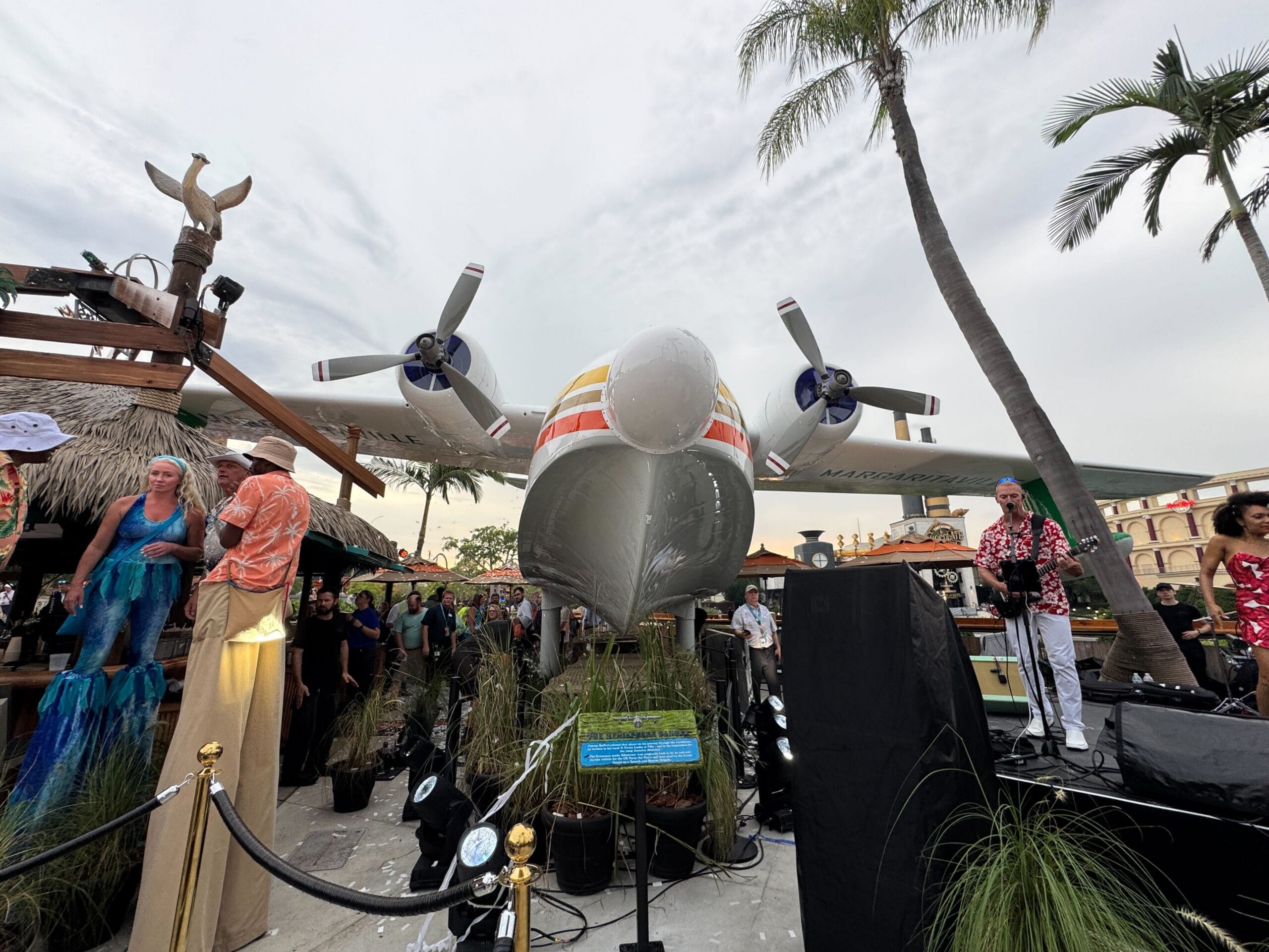 A crowd gathers by the Hemisphere Dancer Plane at Universal CityWalk, surrounded by palm trees and vibrant performers.