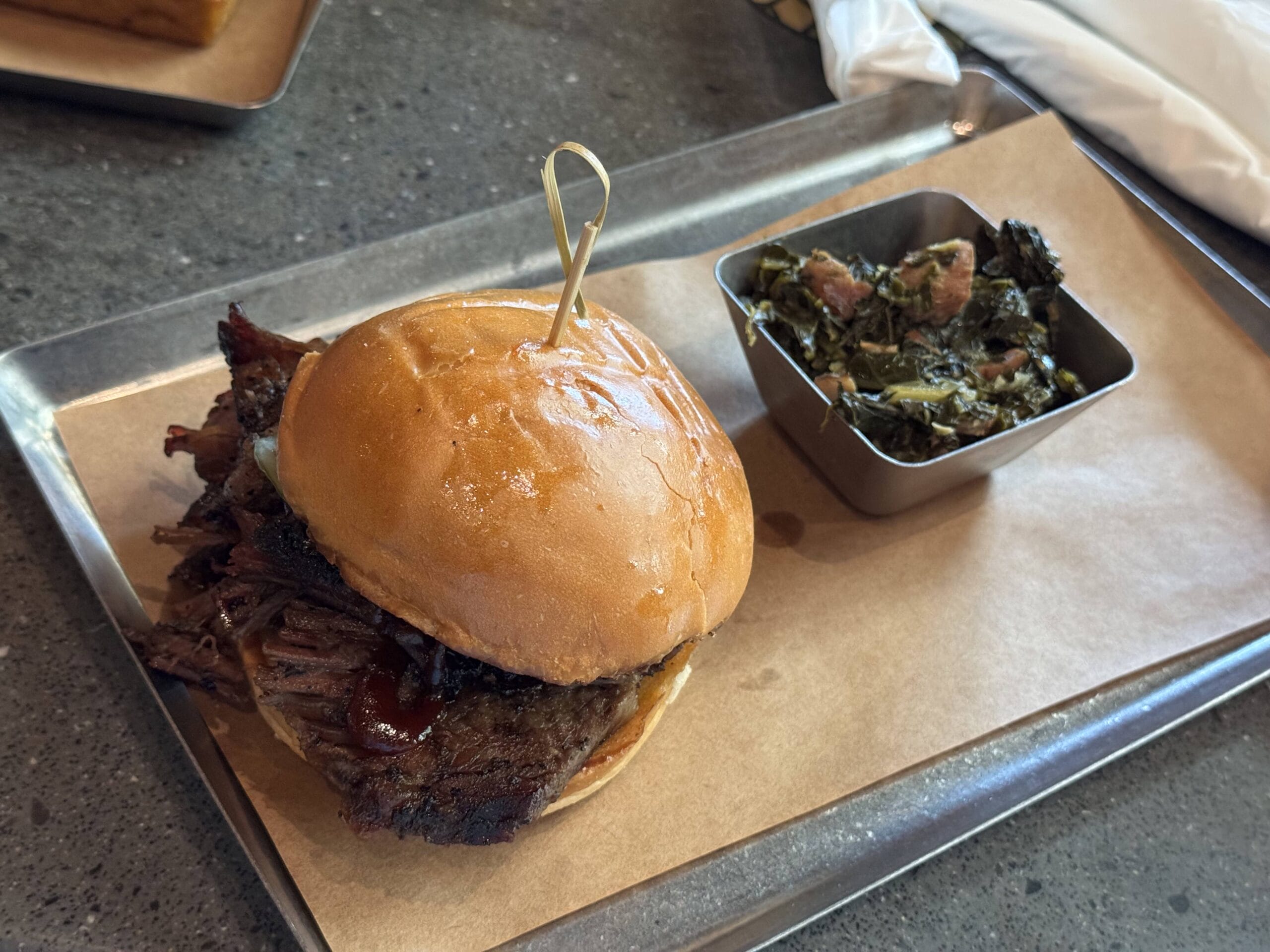 Barbecue beef sandwich on a bun with greens, served at The Oak & Star Tavern on a metal tray lined with parchment paper.